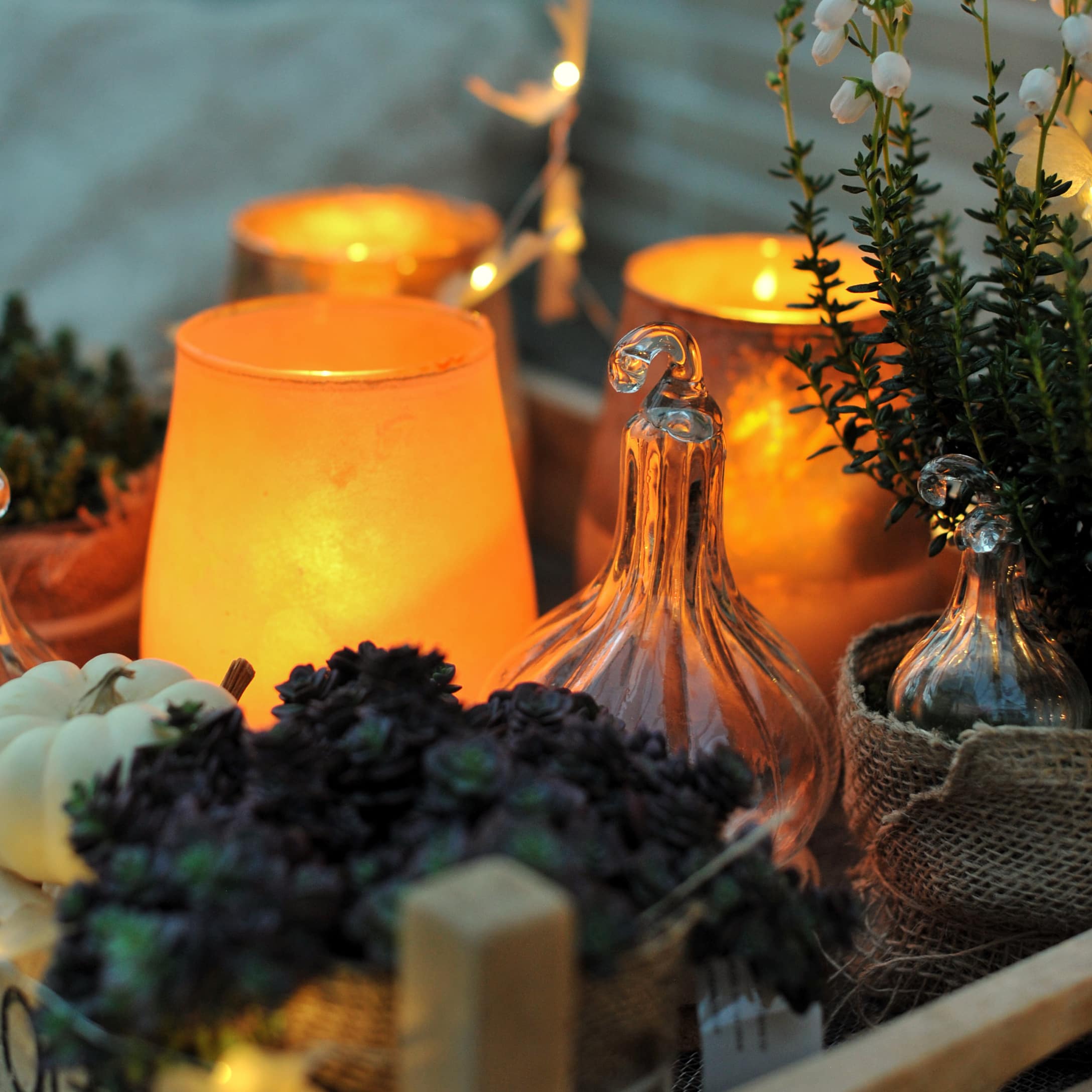 Décor automnal chaleureux avec citrouilles en verre et bougies orange pour ambiance cosy