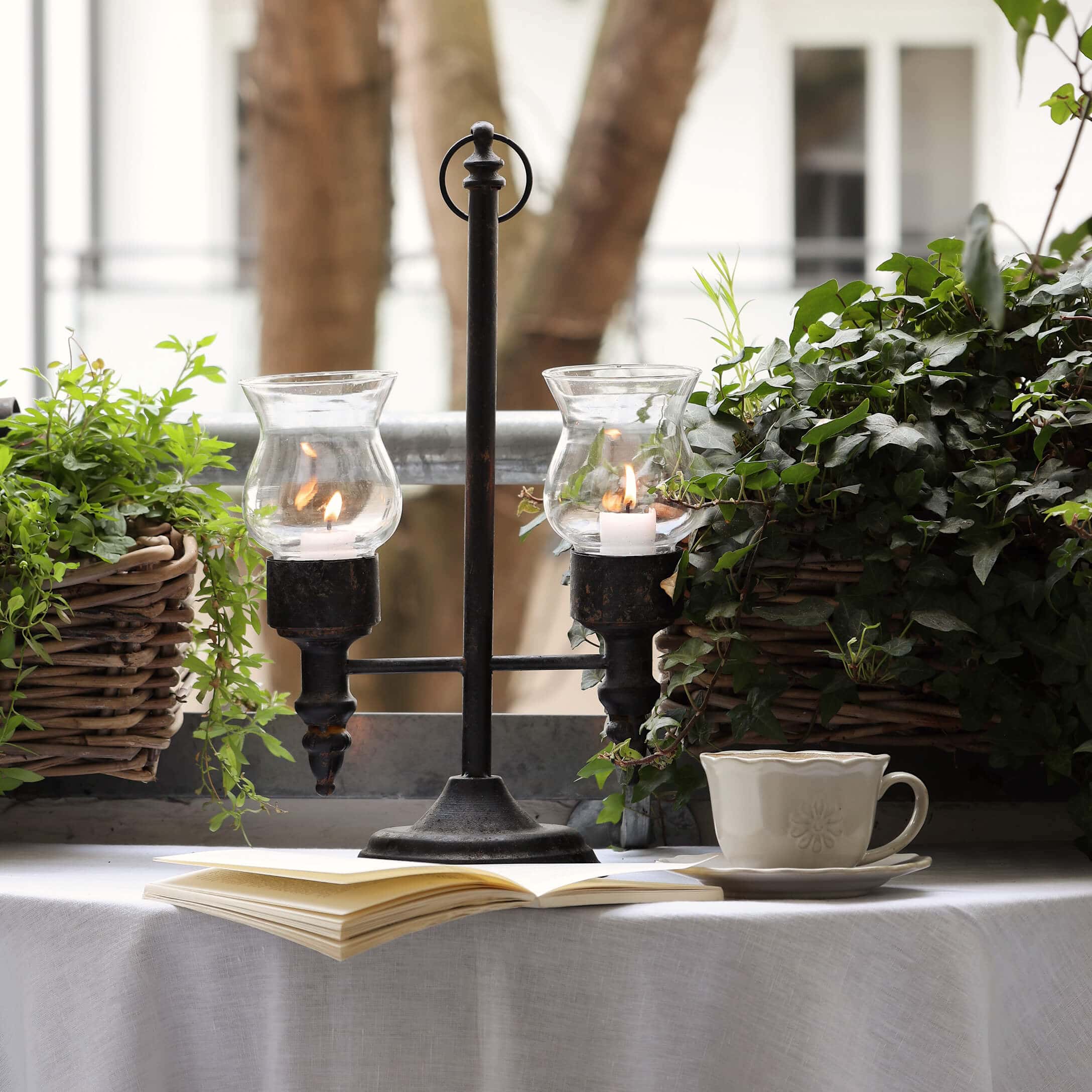 Bougeoir en métal avec deux verres protecteurs entouré de plantes vertes sur un balcon