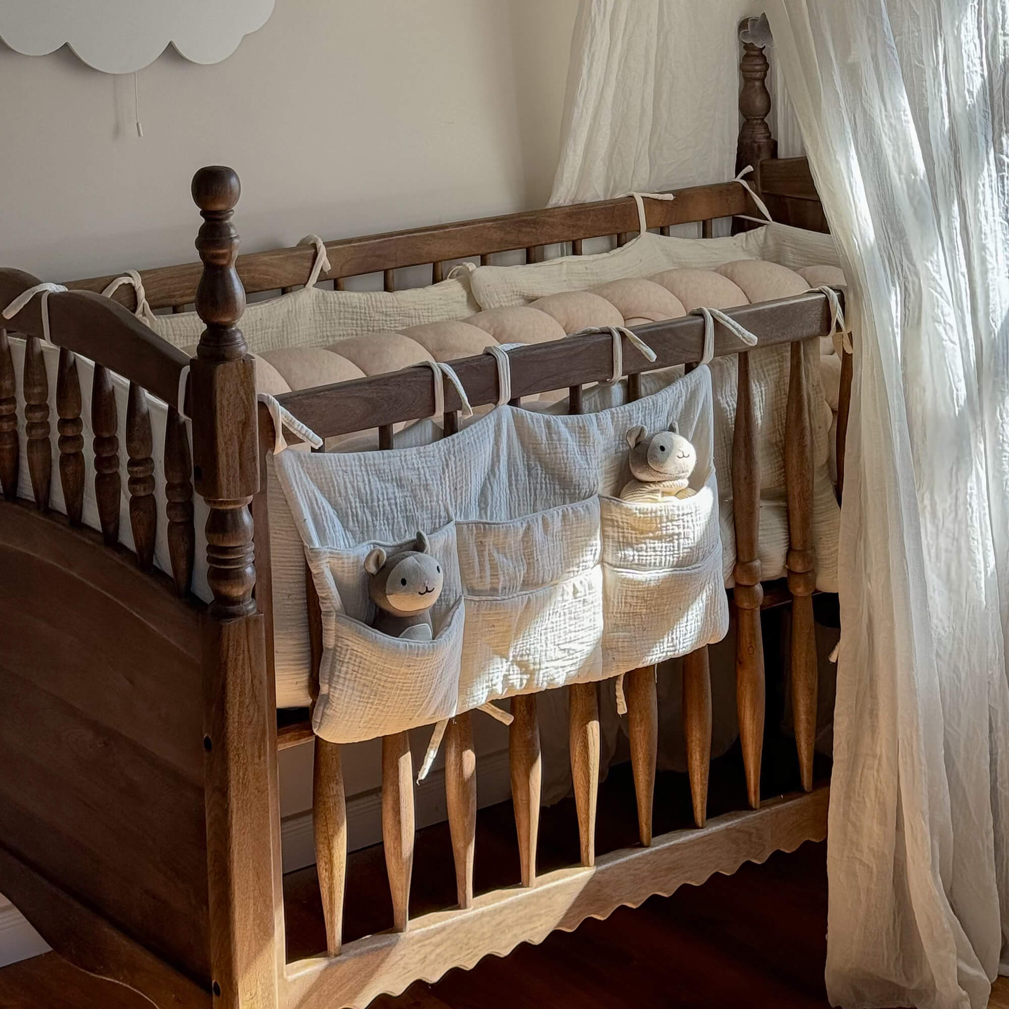 Lit bébé en bois avec protection en coton crème et peluches dans les poches pour chambre enfant