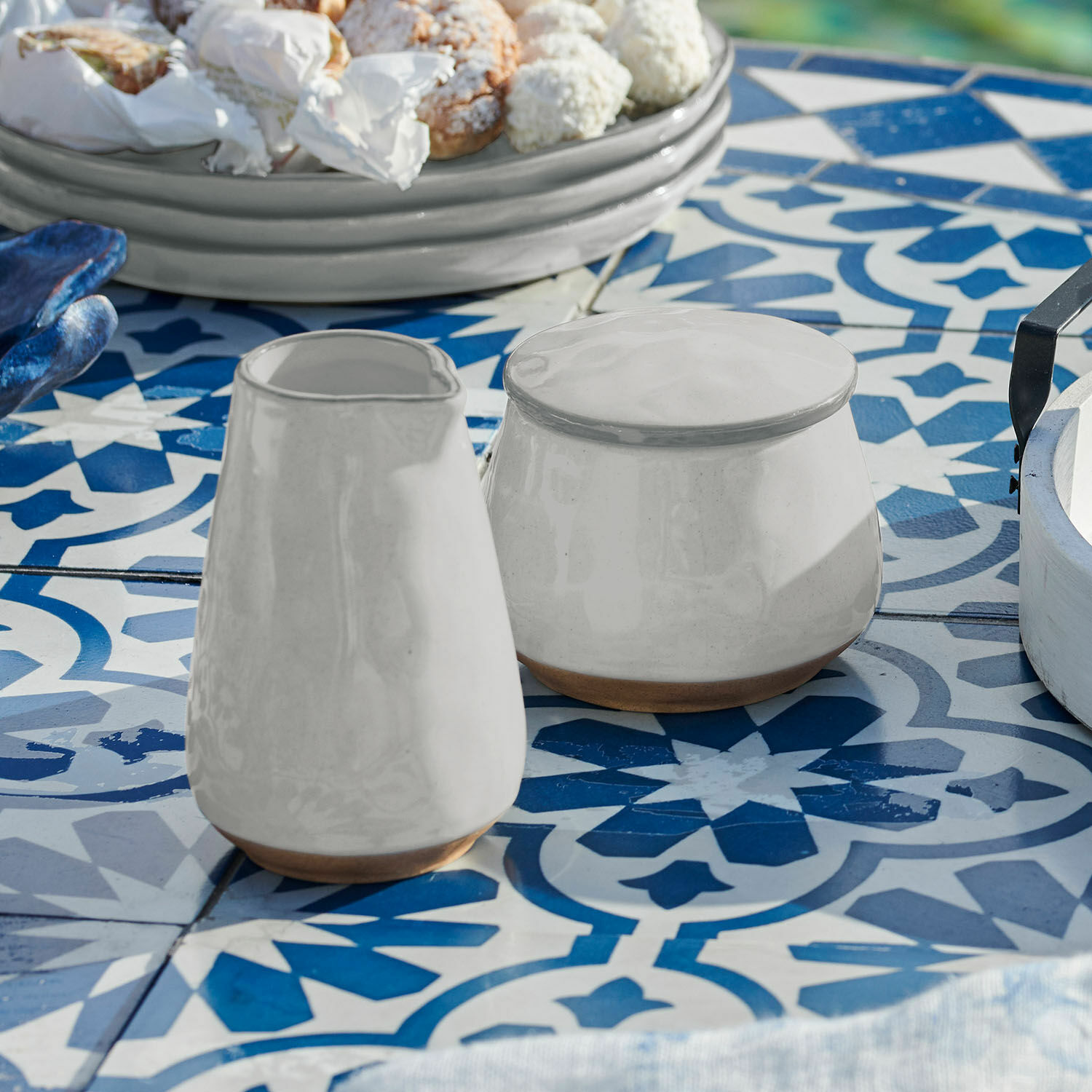 Sucrier et petit pot à lait Biarré Pichet et sucrier en céramique blanche avec base marron naturel sur table à carreaux bleus et blancs