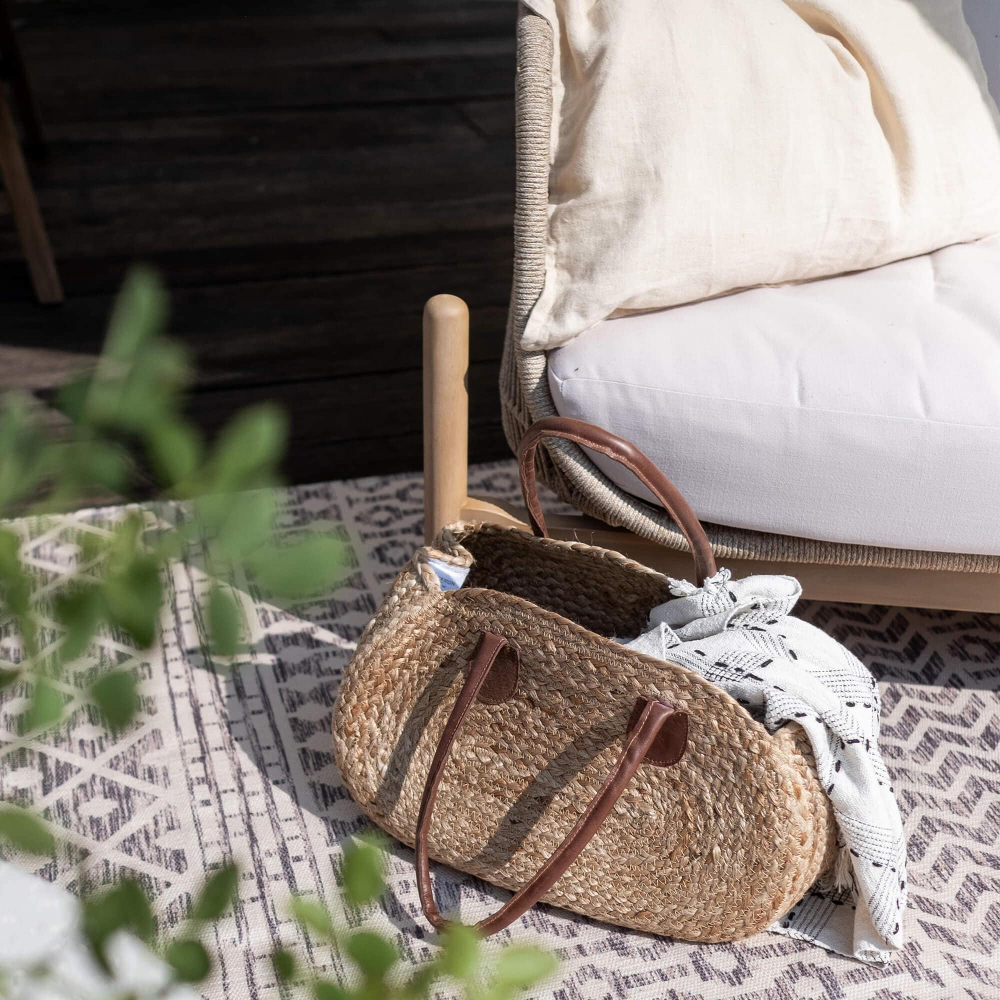 Sac ovale en osier avec poignées marron et tissu blanc posé sur un tapis à motifs géométriques