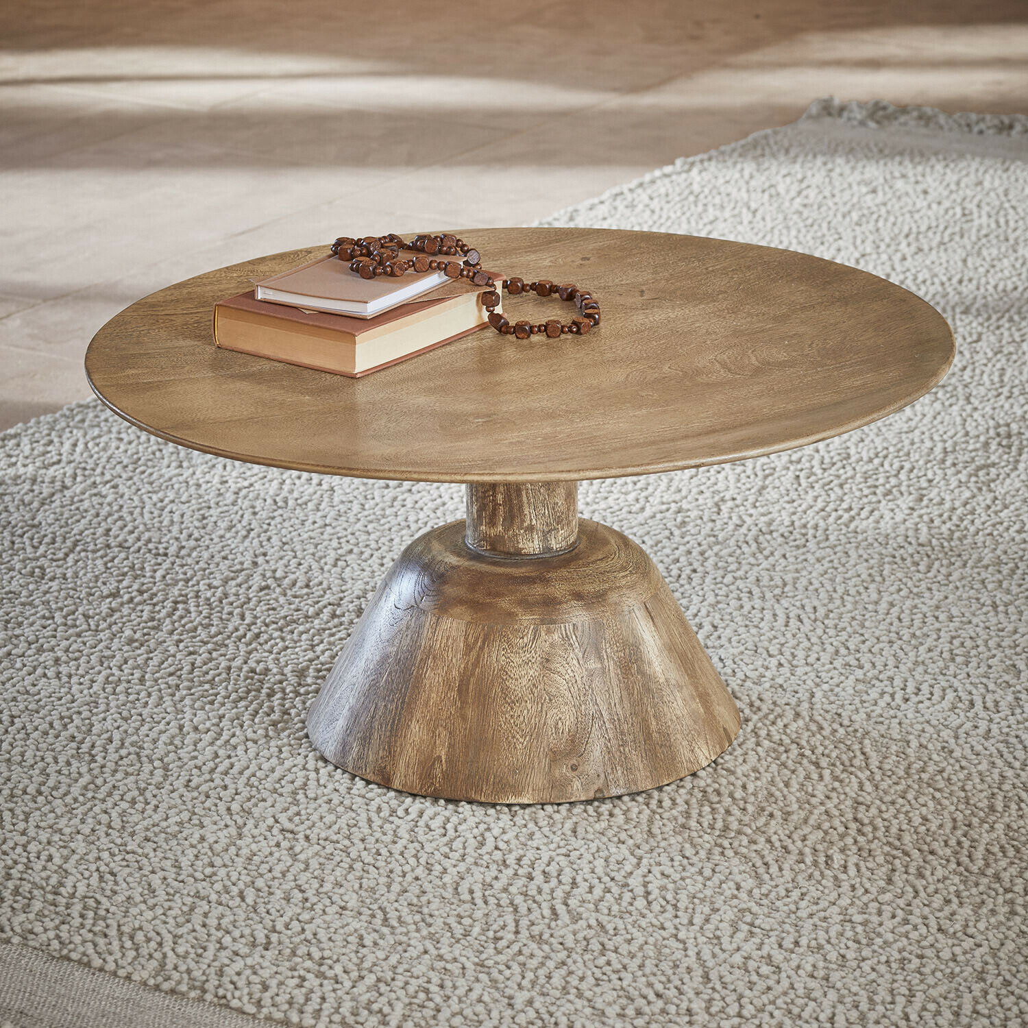 Table basse Ulric Table basse ronde en bois couleur naturelle sur tapis clair avec livres et collier en perles