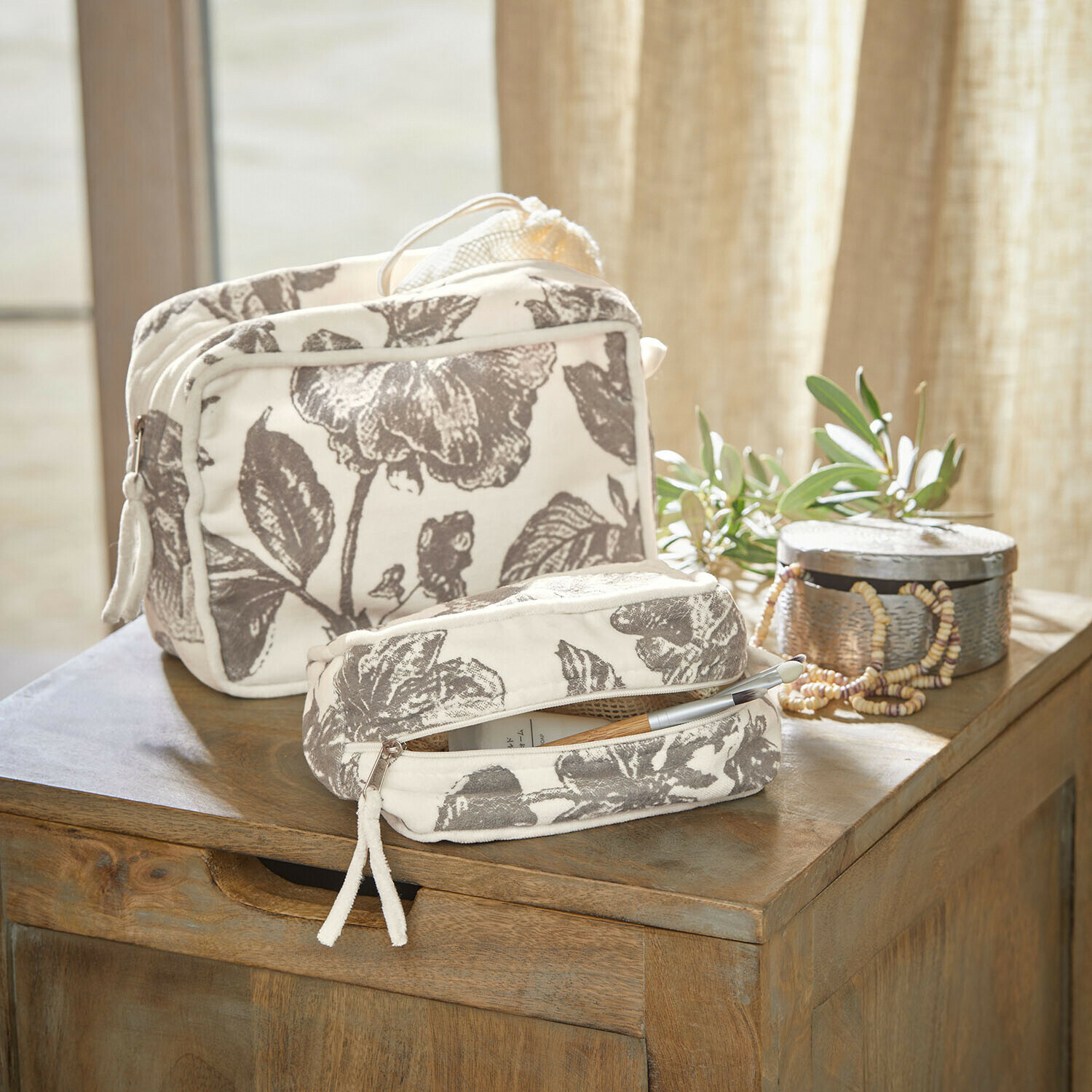 Lot de 2 pochettes Brilonne Ensemble de deux trousses en coton crème avec motif floral gris posées sur une table en bois