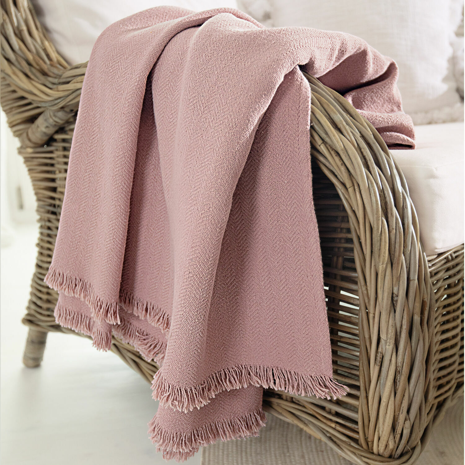Plaid Herepian Plaid rose en tissu doux avec franges posé sur un fauteuil en osier pour salon cosy