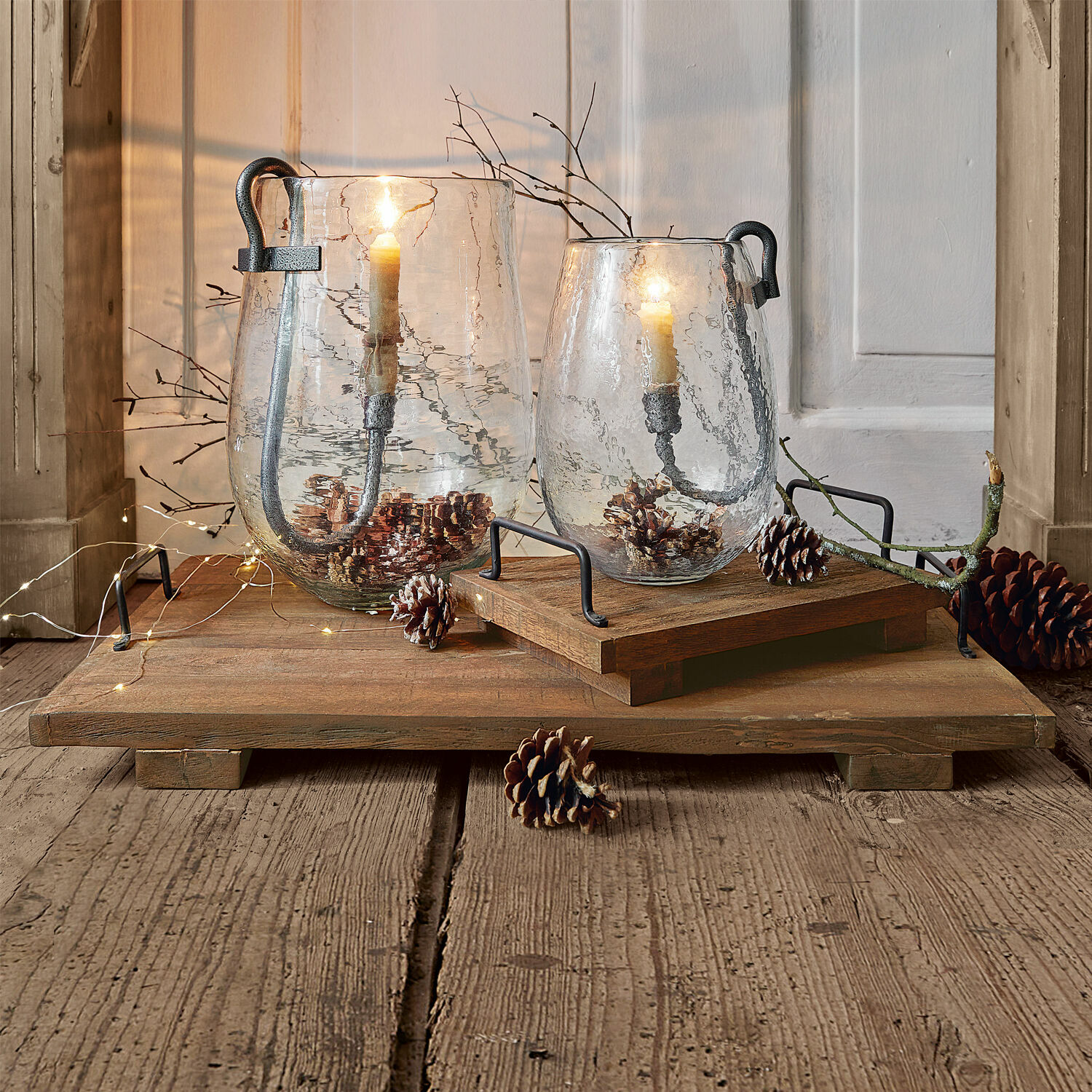 Lot de 2 plateaux Conner Lanterne en verre avec poignées en métal sur plateau en bois, décorée de pommes de pin et bougies allumées