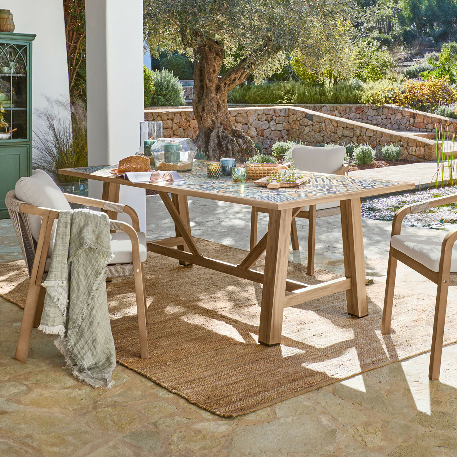 Table de jardin avec plateau en mosaïque et cadre en bois sur terrasse avec chaises et tapis naturel