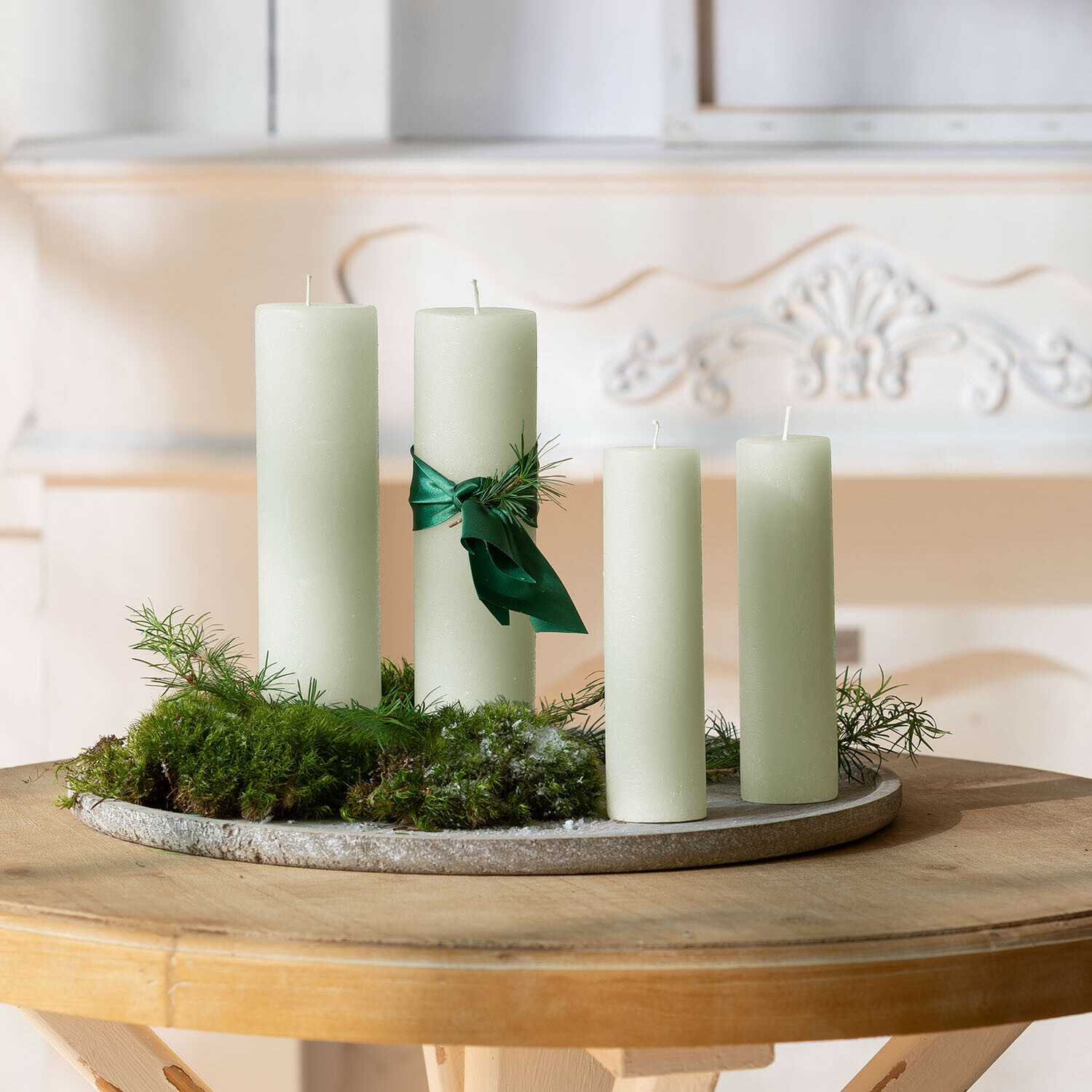 Lot de 4 bougies Avinal Ensemble de quatre bougies crème avec ruban vert et mousse sur un plateau décoratif rond