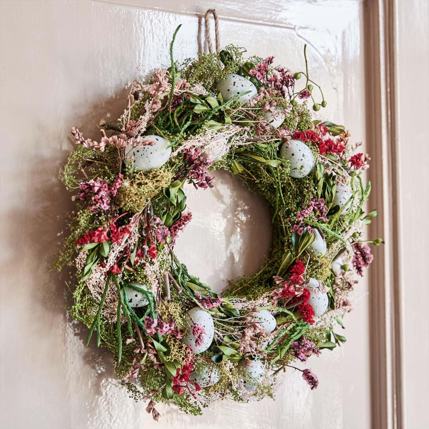 Couronne décorative en branches vertes, fleurs roses et œufs bleus artificiels accrochée à une porte