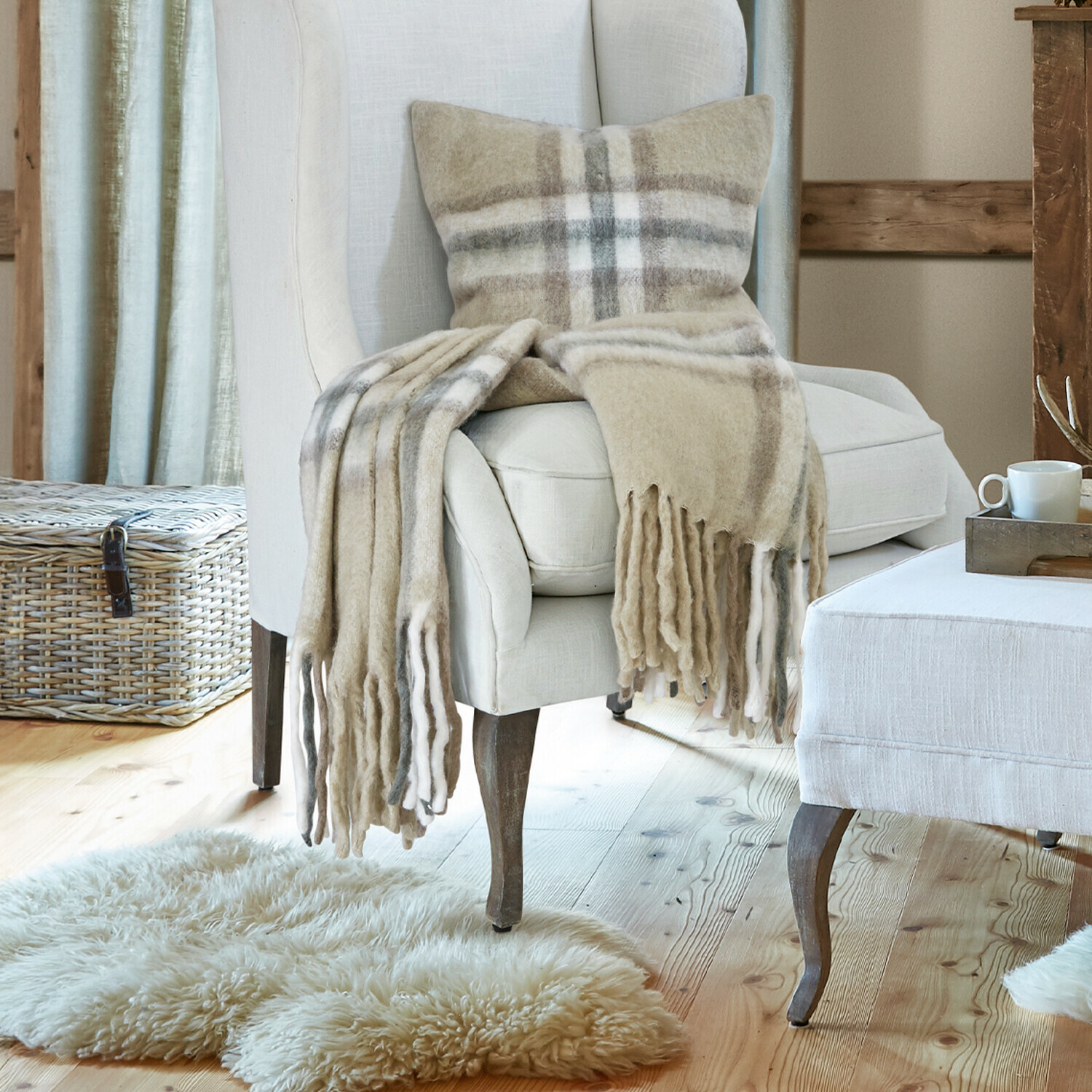Plaid Klinas Fauteuil beige en tissu avec repose-pieds dans un salon chaleureux avec parquet en bois et cheminée