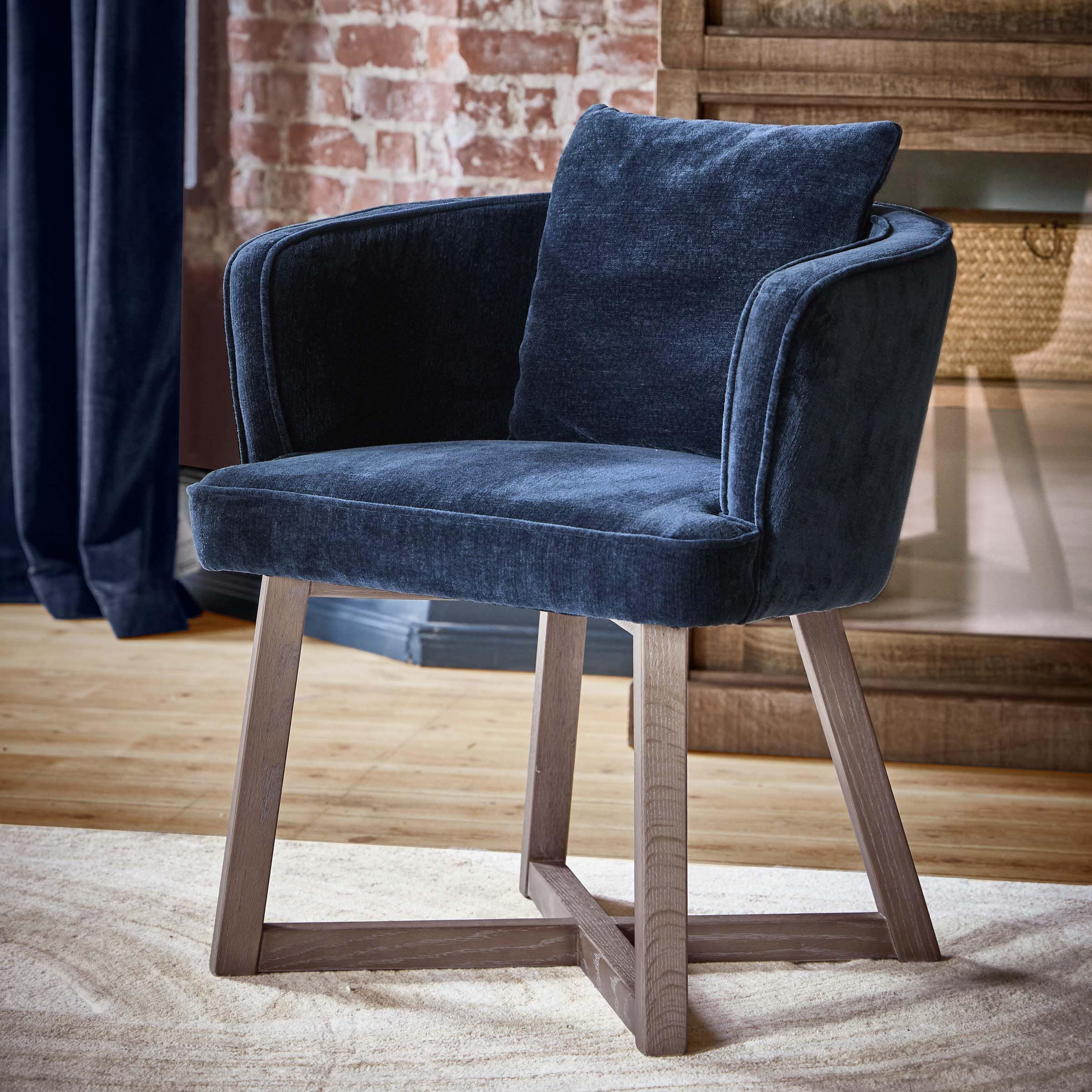 Fauteuil bleu marine en tissu doux avec pieds en bois dans un intérieur élégant avec mur en briques