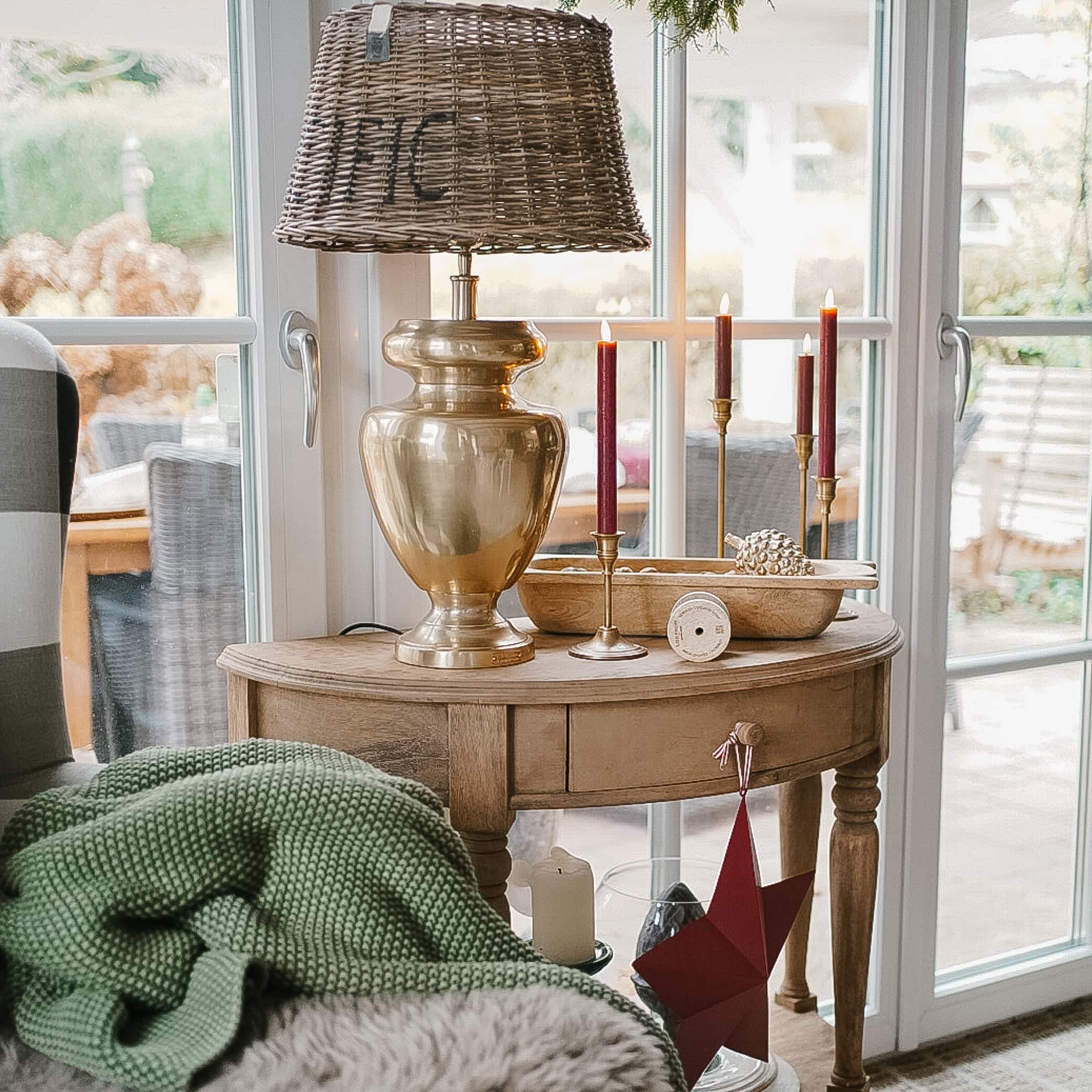 Table en bois avec lampe en laiton et bougies rouges, décorations de Noël dans un salon lumineux