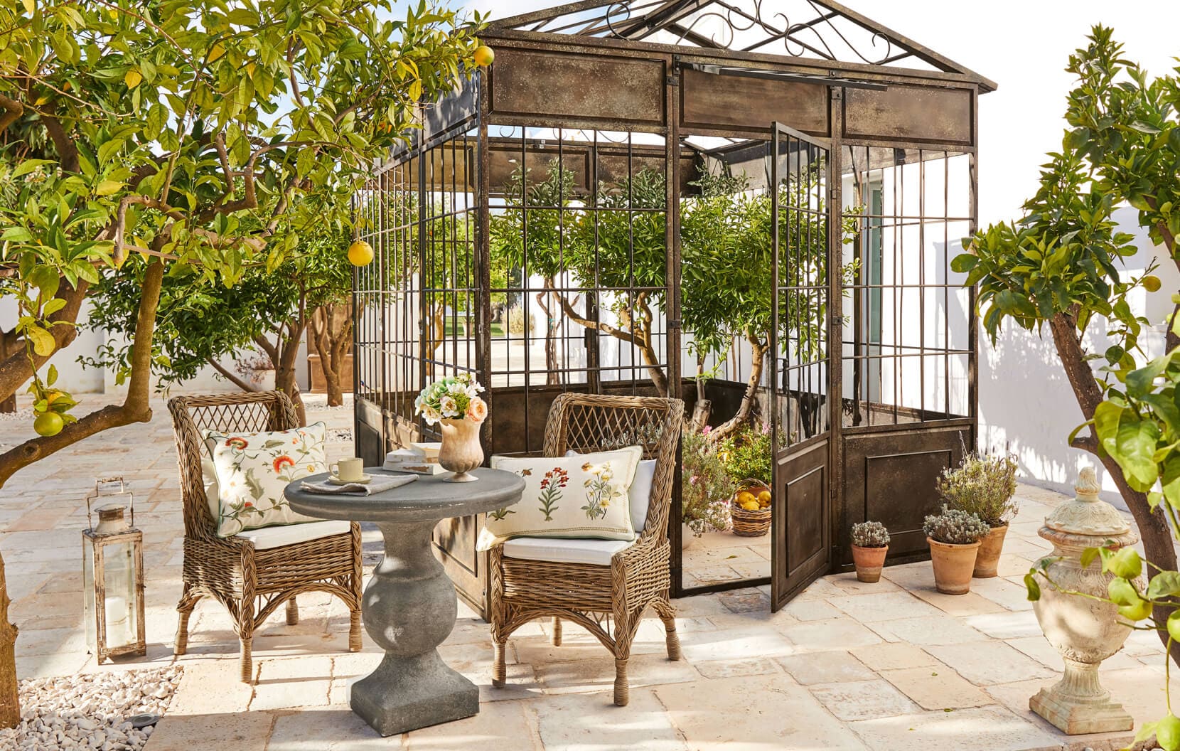 Jardin méditerranéen avec tonnelle en métal, fauteuils en osier et table en pierre sur la terrasse