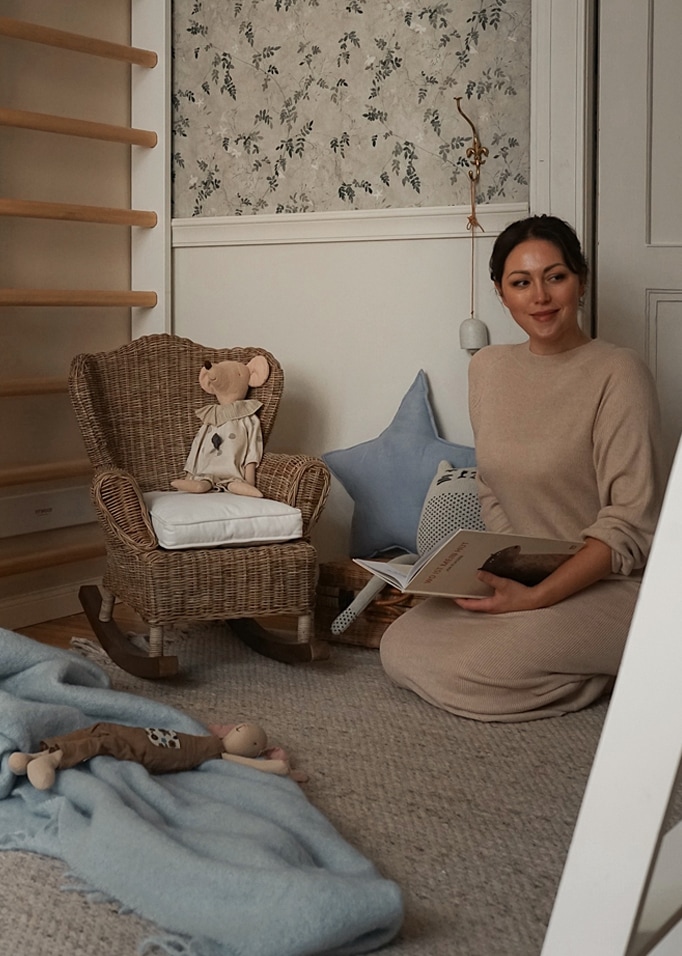 Femme lisant un livre dans une pièce chaleureuse avec fauteuil à bascule en osier et peluches