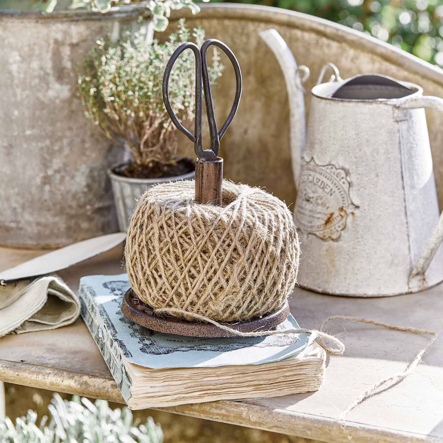 Bobine de ficelle en jute naturelle sur support métallique avec ciseaux dans un décor de jardin rustique