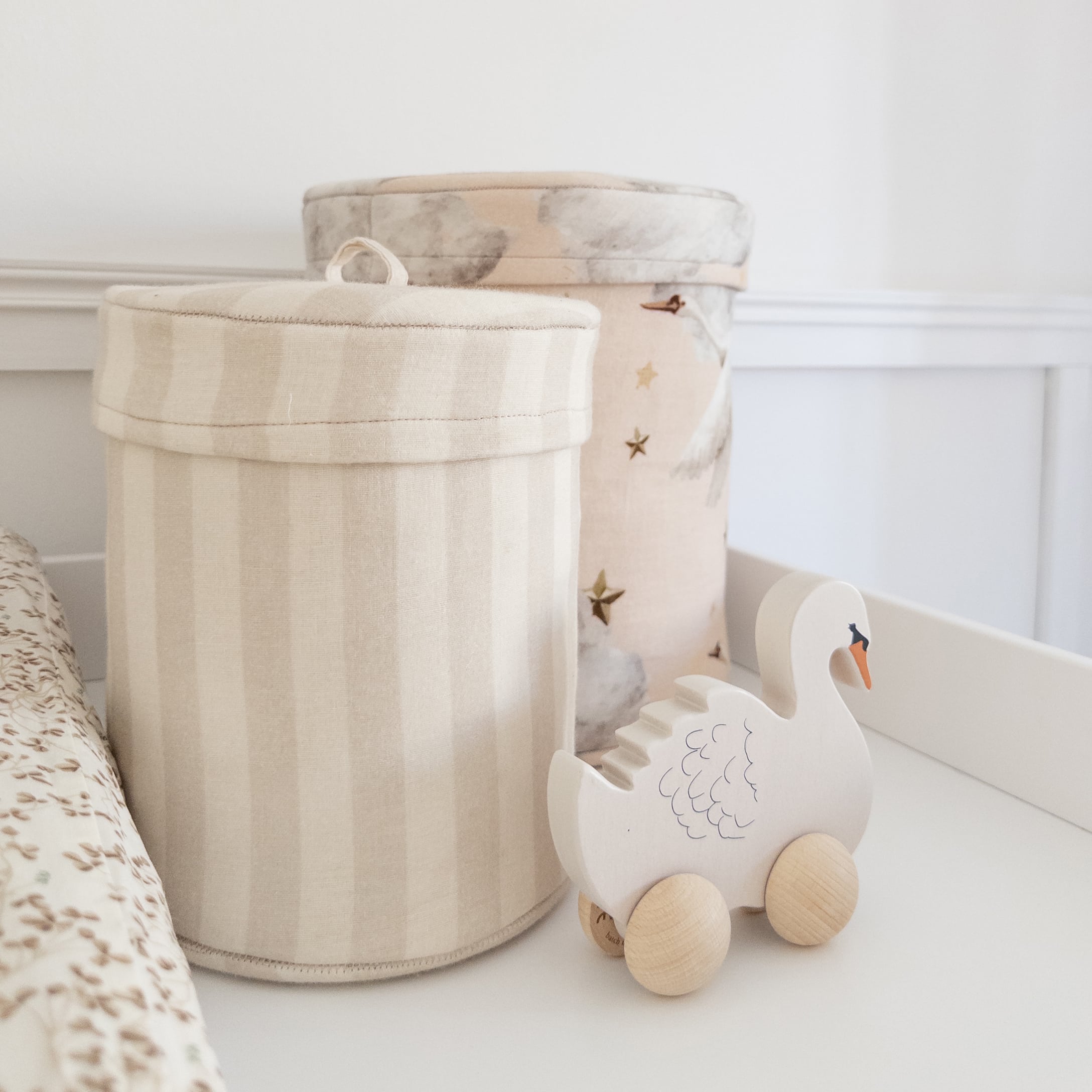 Jouet cygne en bois sur roues à côté de boîtes en tissu beige dans une chambre d'enfant
