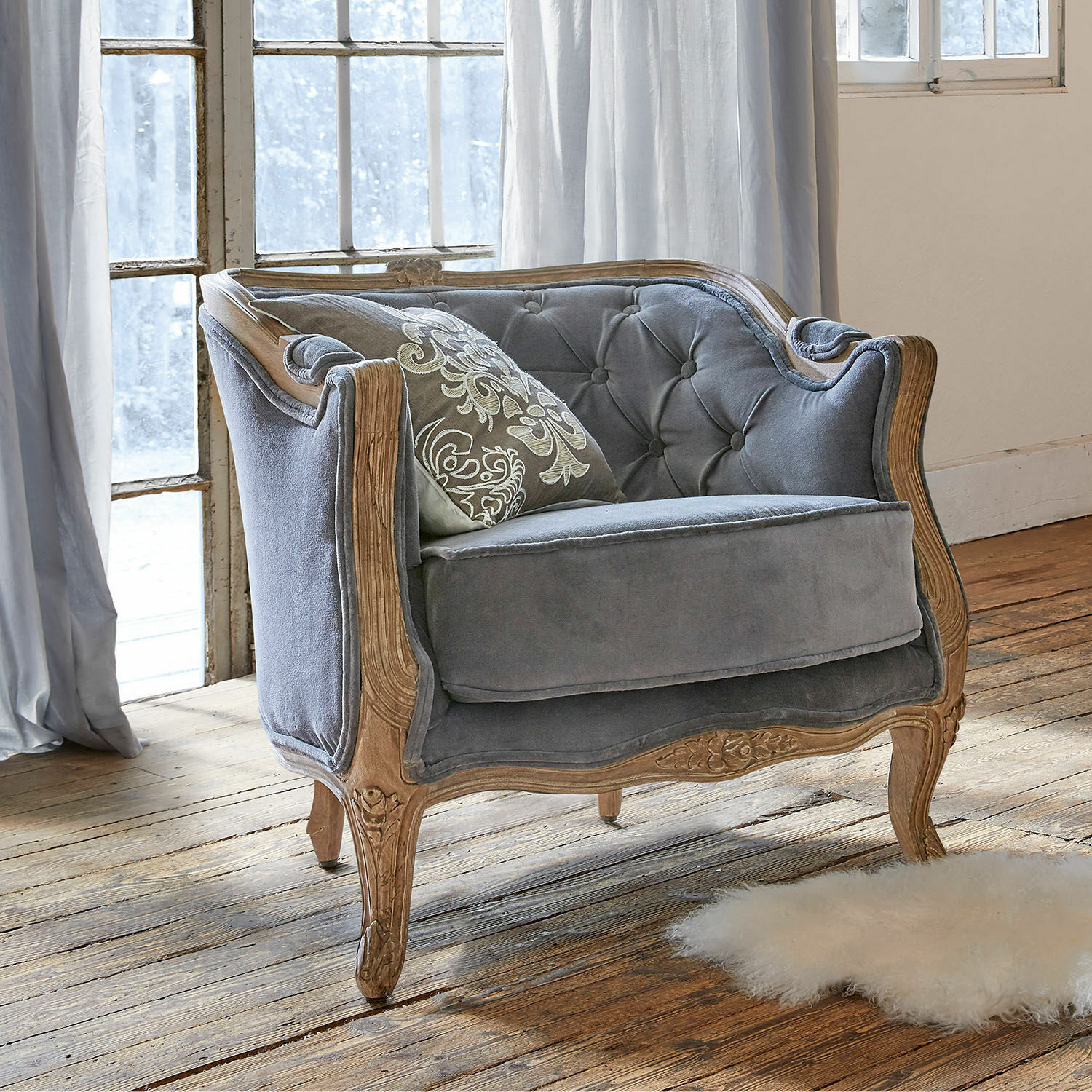 Fauteuil Annezay Canapé gris en velours avec cadre en bois sculpté sur un sol en bois dans une pièce lumineuse