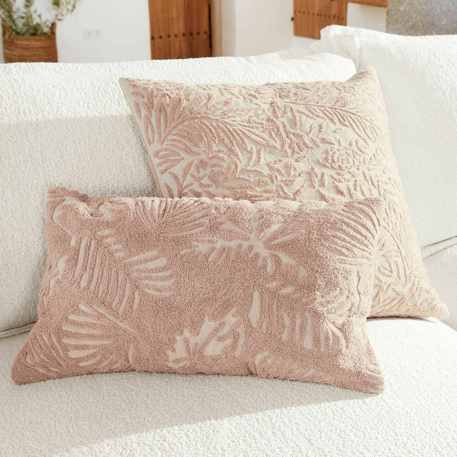 Lot de 2 housses de coussin Enchanto Deux coussins décoratifs avec motif de feuilles roses sur fond crème posés sur un canapé blanc