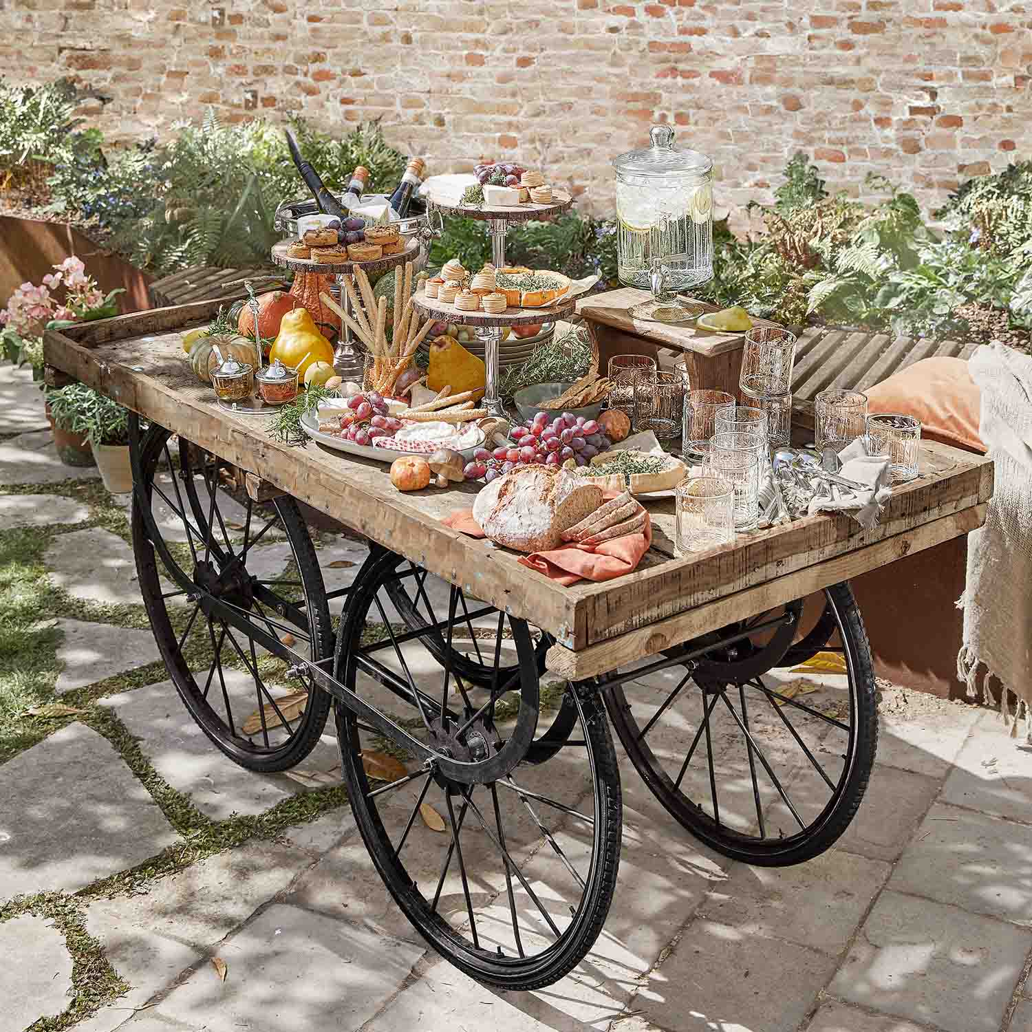 Chariot en bois rustique avec roues noires chargé de snacks et boissons dans un jardin ensoleillé