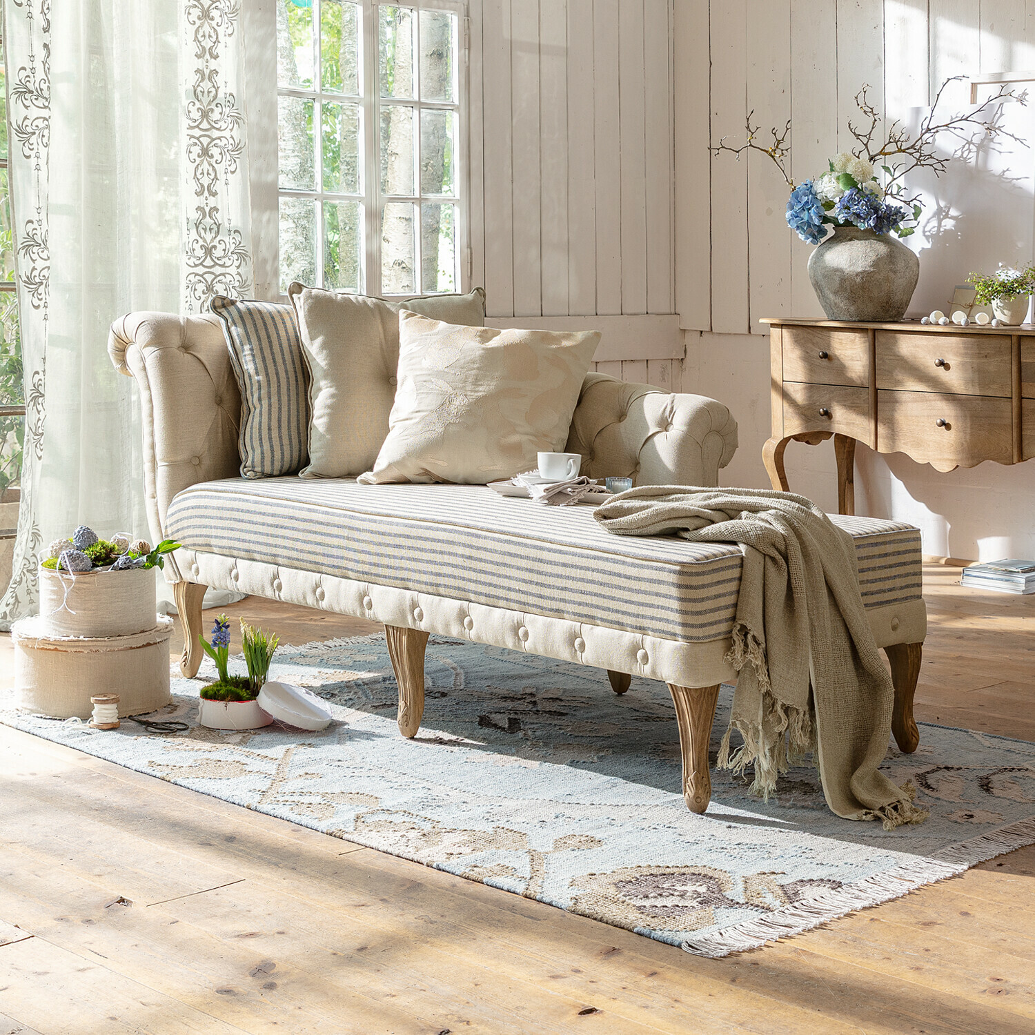 Méridienne Viviani Canapé capitonné beige avec pieds en bois et assise rayée dans un salon lumineux décoré avec des coussins