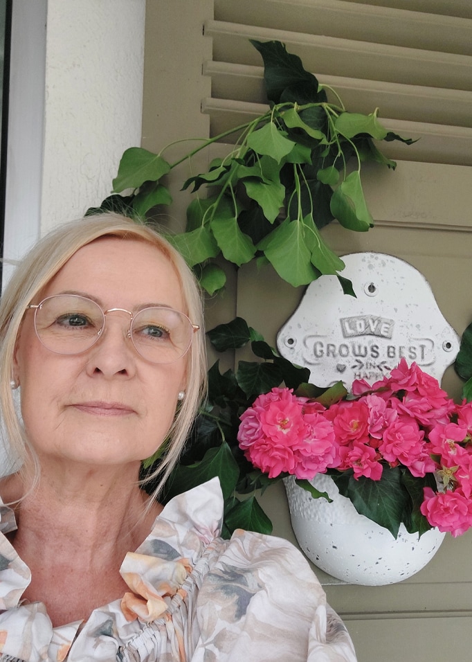 Pot en céramique blanc avec fleurs roses et feuilles vertes devant des volets gris