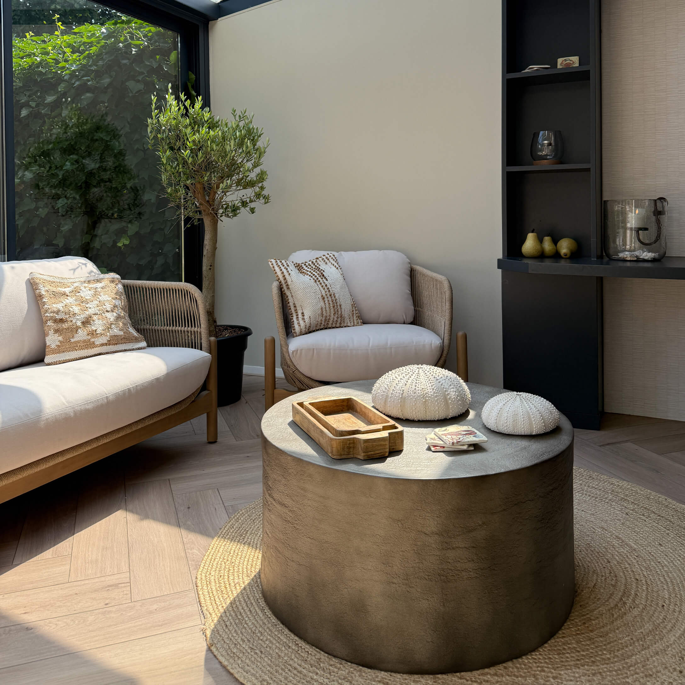 Salon moderne avec canapé beige et fauteuil en tissu, table basse en béton sur tapis rond naturel