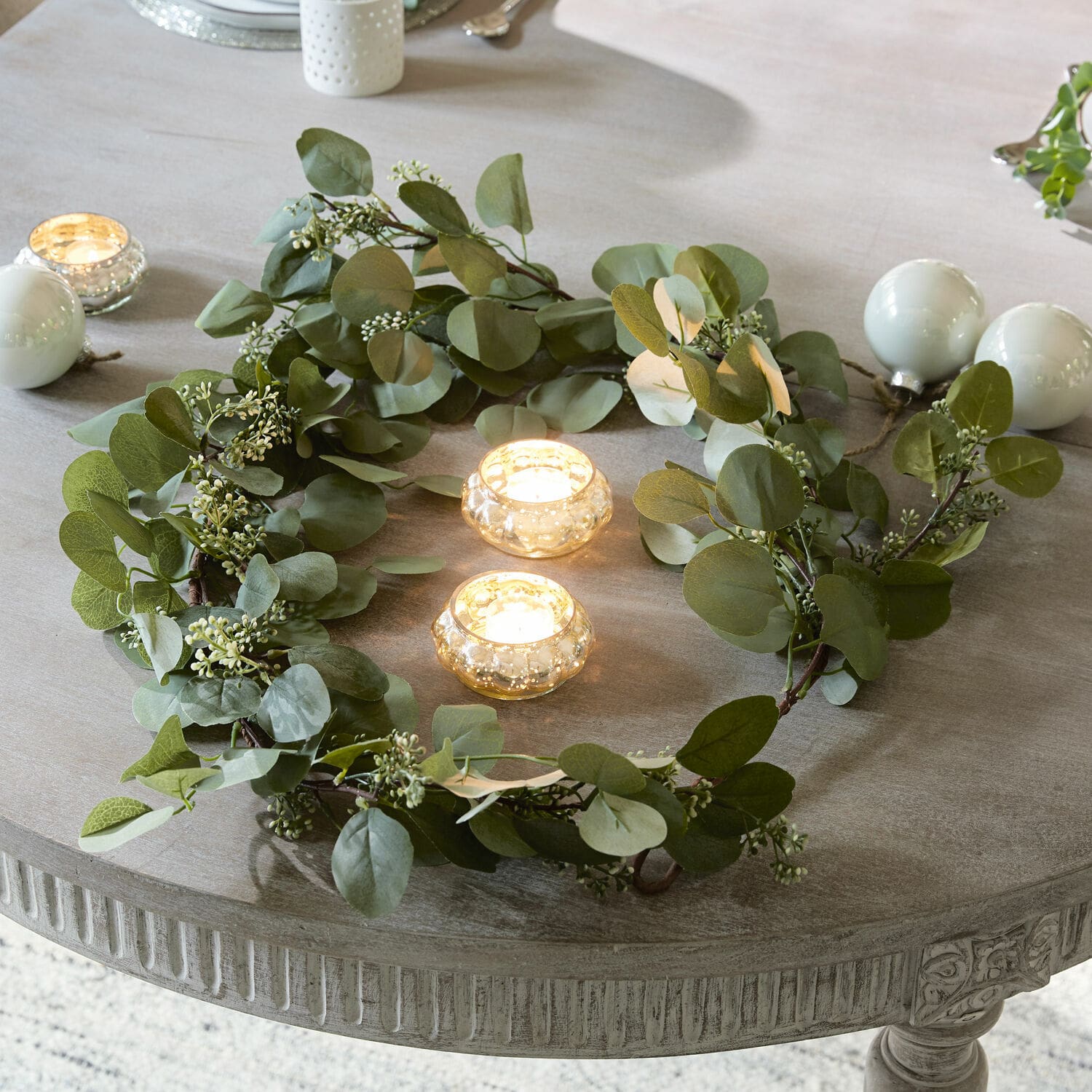 Guirlande Xantos Couronne décorative de feuilles vertes sur une table grise avec deux bougies dans des photophores en verre