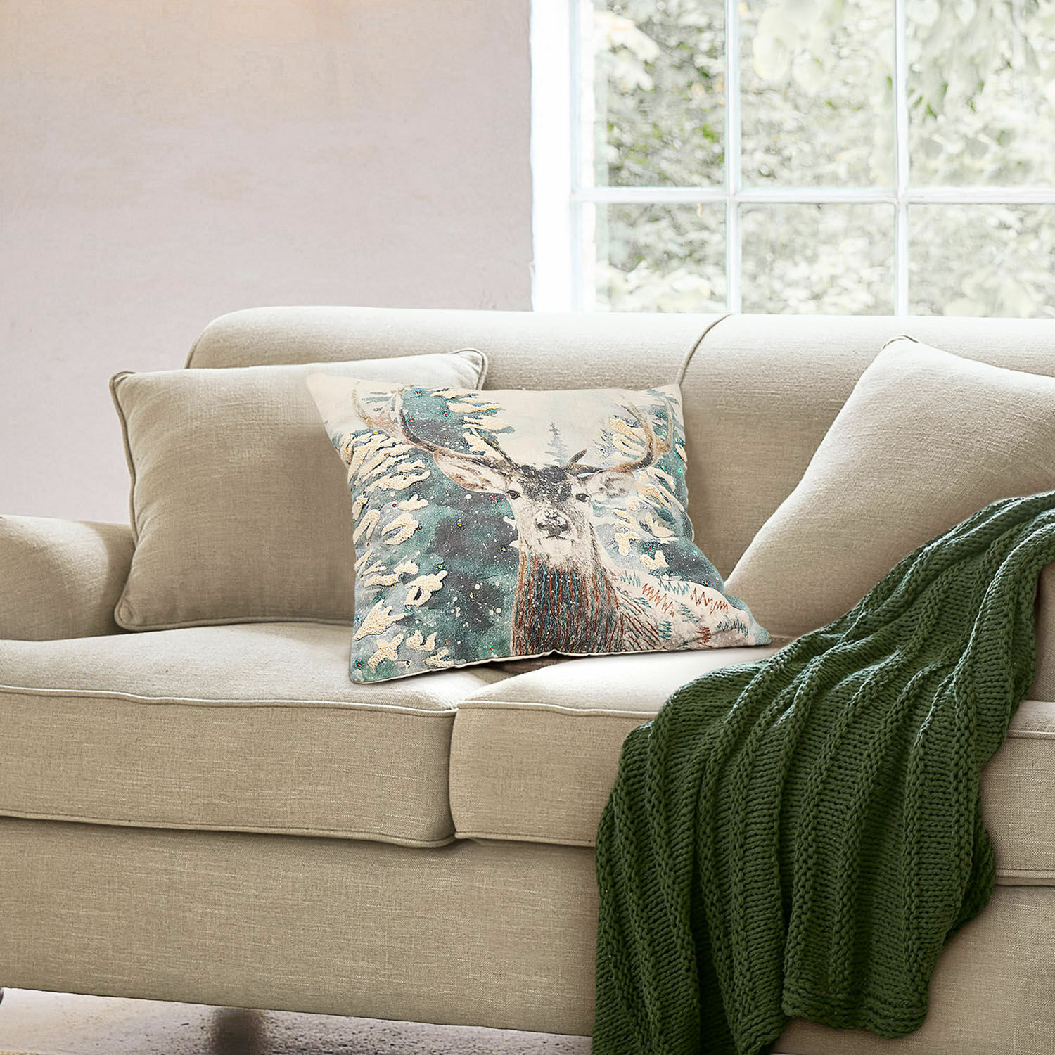 Housse de coussin Elvaris Canapé beige avec coussin décoratif motif cerf et plaid vert tricoté dans un salon lumineux