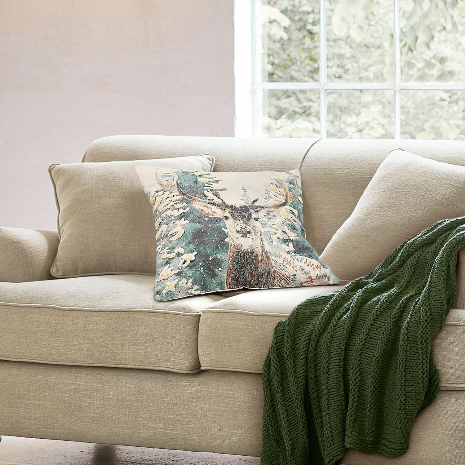Housse de coussin Elvaris Canapé beige avec coussin décoratif motif cerf et plaid vert tricoté dans un salon lumineux