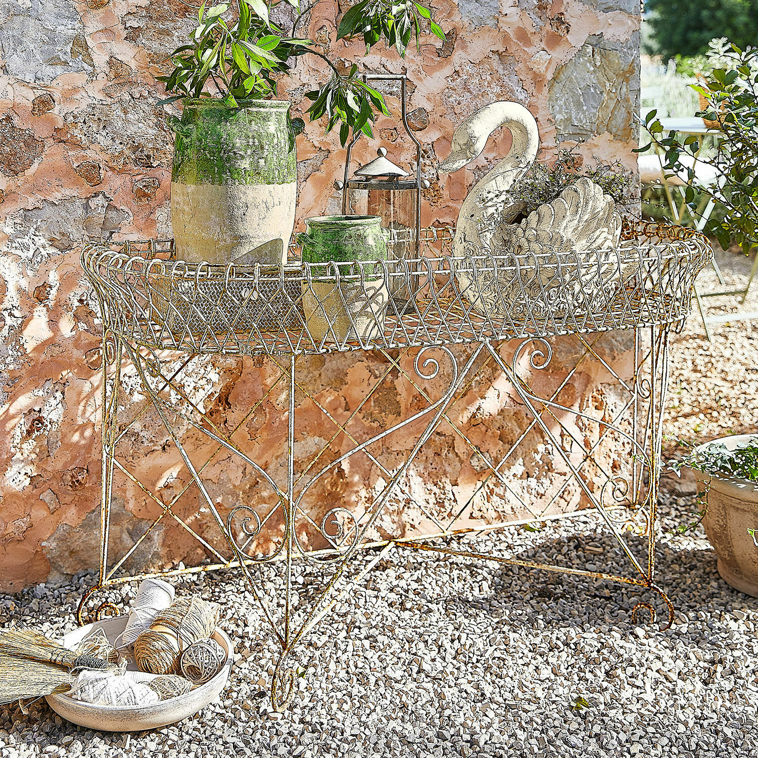 Étagère à plantes Pacentro Table de jardin en métal rustique avec pots décoratifs et ornement cygne devant un mur en pierre