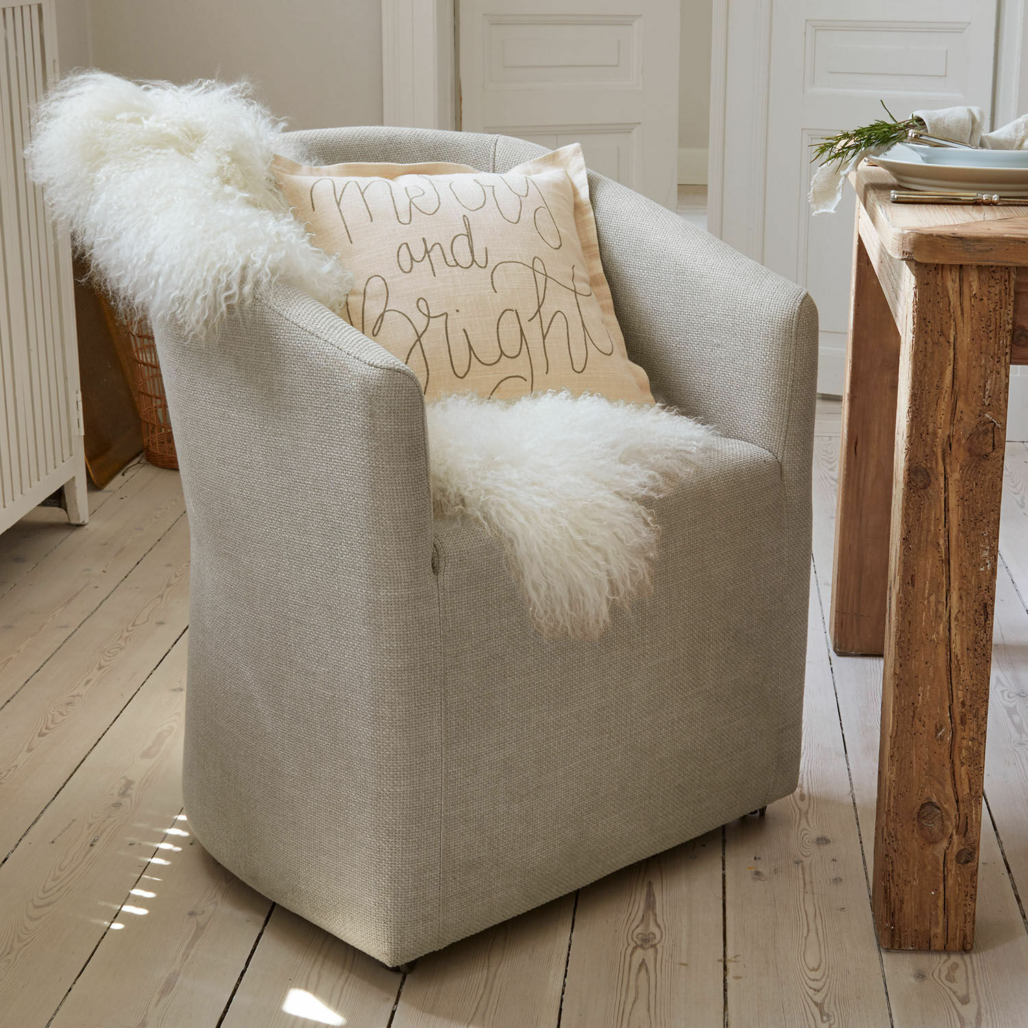 Fauteuil Holmsen Fauteuil gris en tissu avec couverture blanche douce et coussin décoratif clair dans un intérieur scandinave