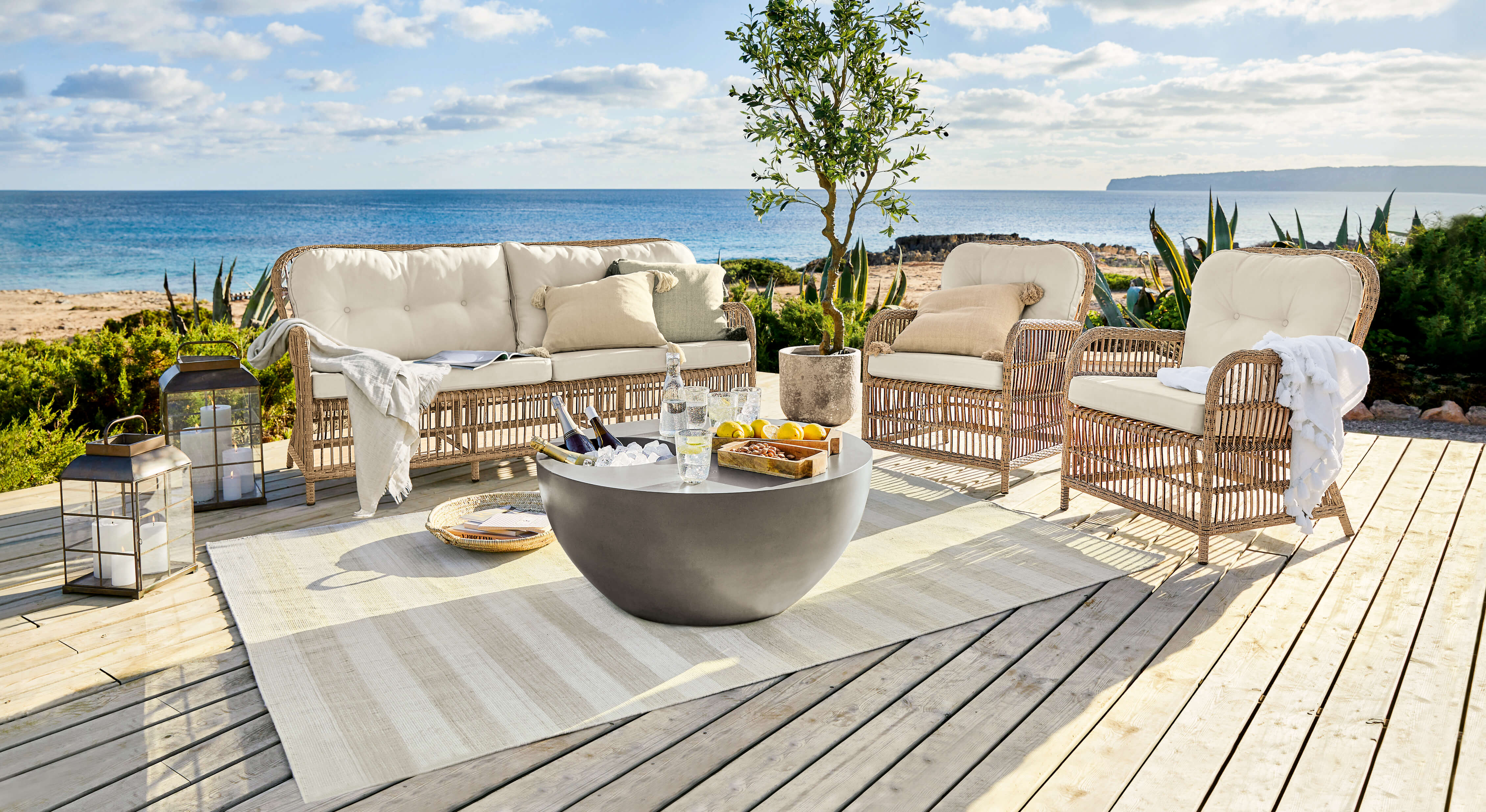 Ensemble de meubles de jardin en rotin avec coussins crème sur terrasse en bois face à la mer