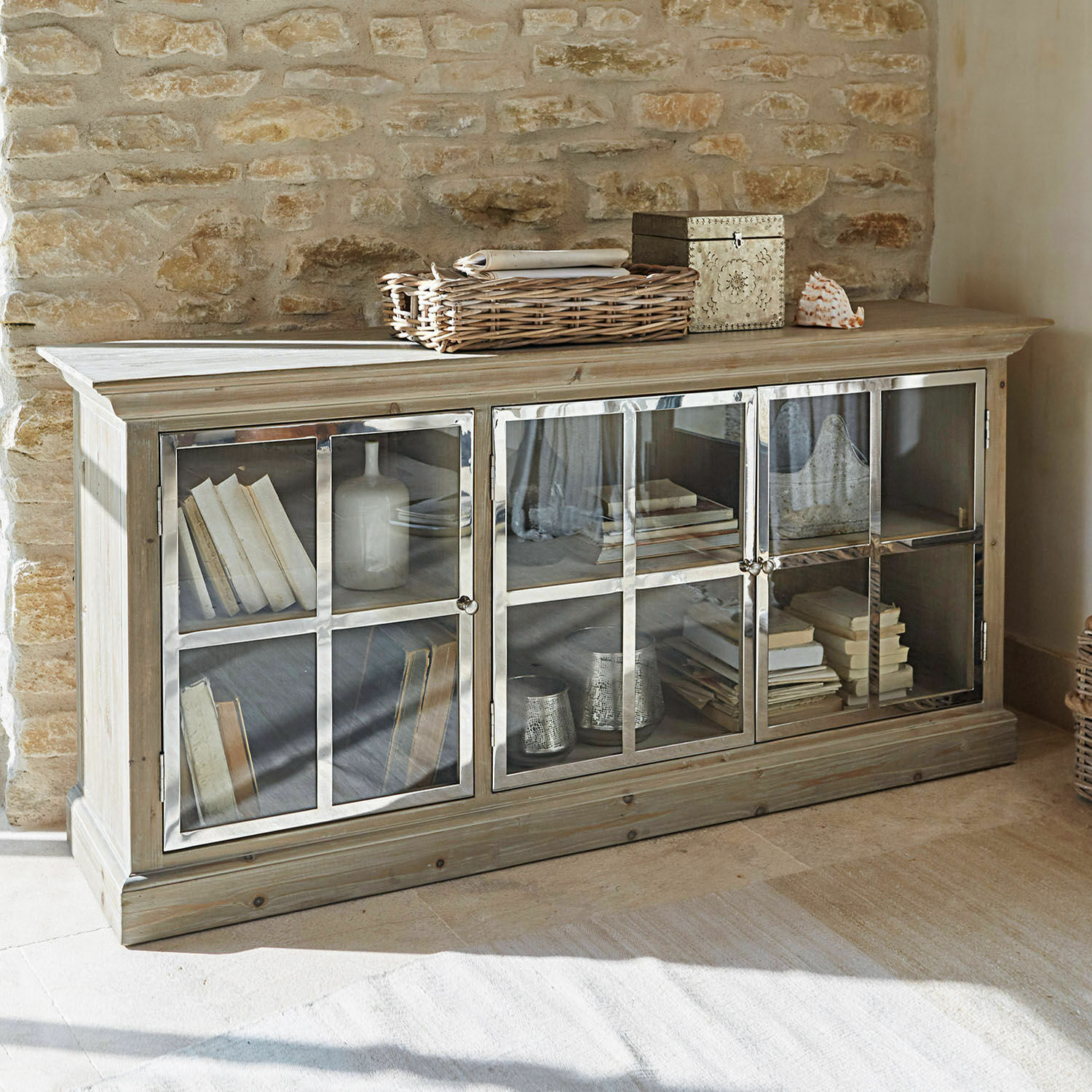 Buffet bas Keyport Buffet en bois clair à trois portes vitrées avec livres et décorations dans un intérieur rustique