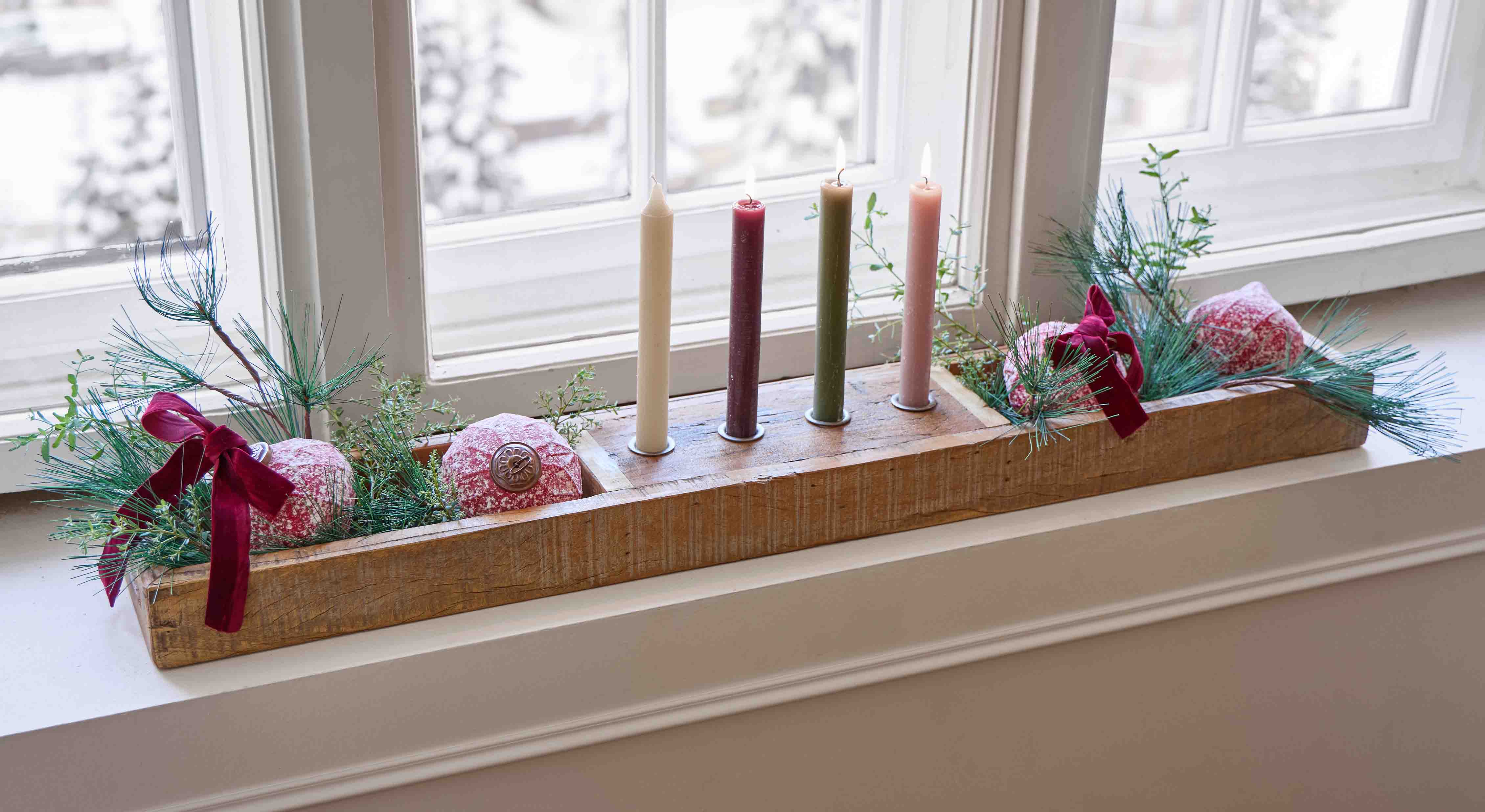 Bougeoir en bois avec quatre bougies colorées et décorations vertes et rouges sur rebord de fenêtre