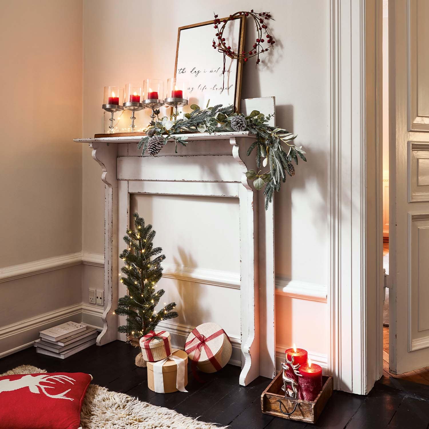 Cheminée blanche en bois décorée pour Noël avec bougies rouges et cadeaux emballés au sol