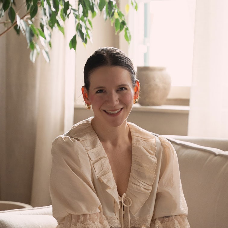 Femme souriante en blouse crème à volants assise sur un canapé dans un intérieur lumineux et chaleureux