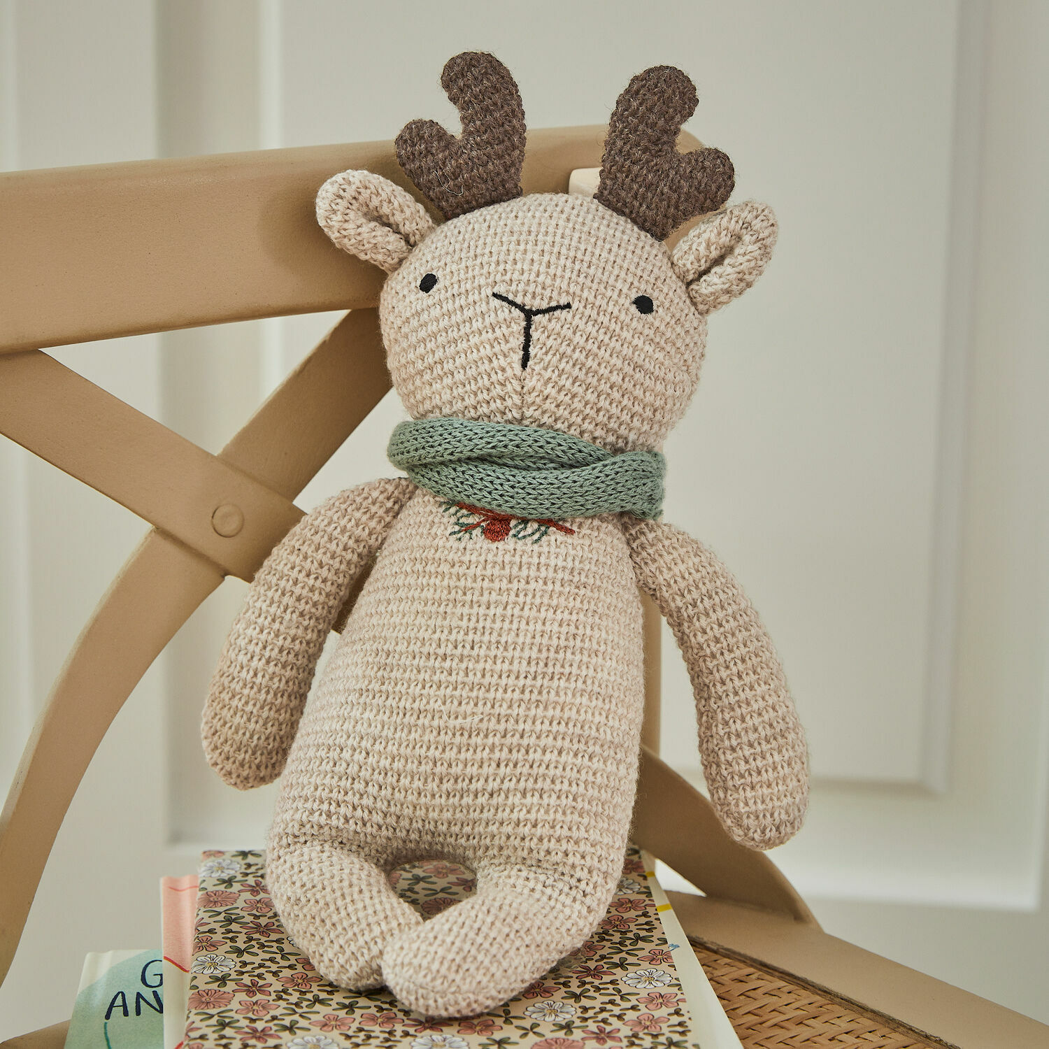 Peluche Papillia Jouet renne tricoté beige avec bois marron et écharpe verte posé sur une chaise