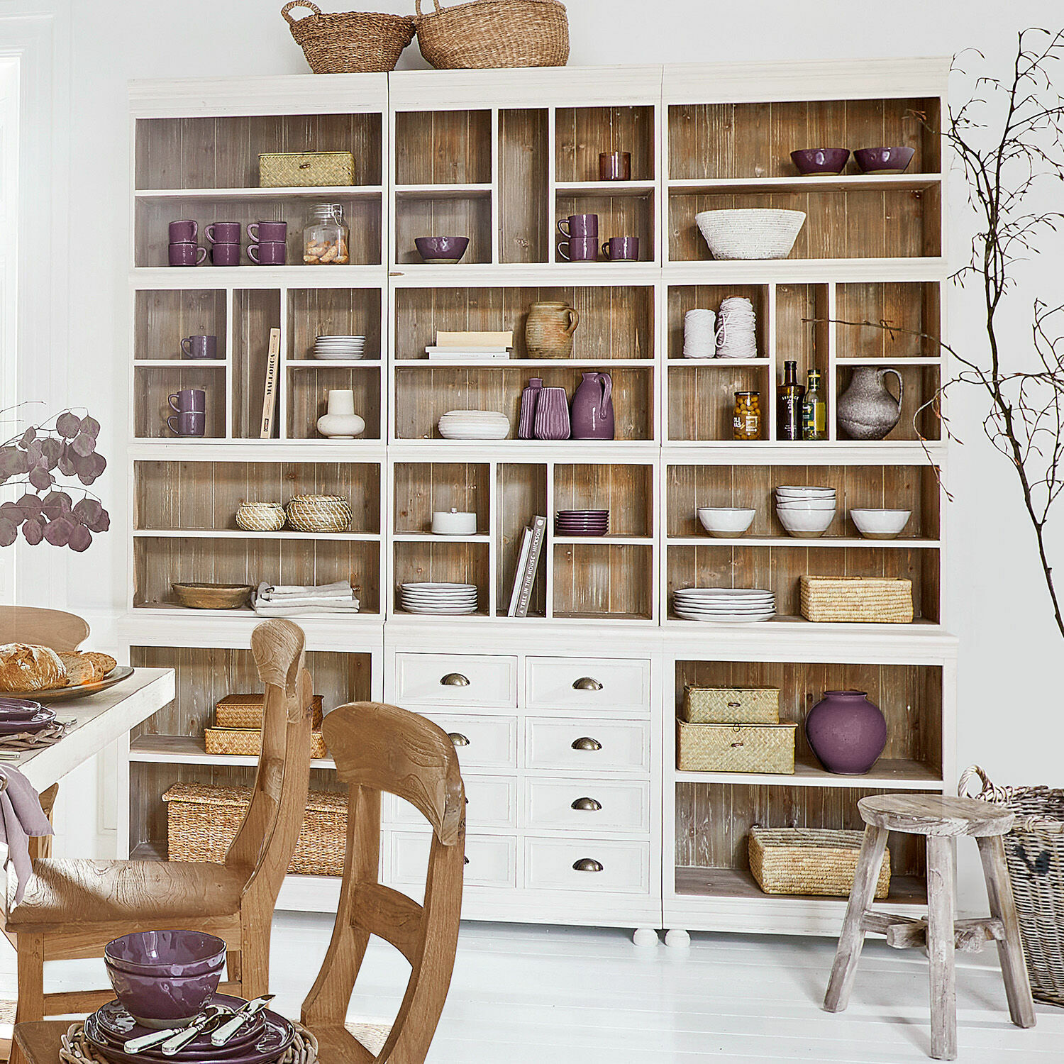 Vitrine en bois blanc avec étagères et tiroirs, décorée de céramiques violettes et paniers en osier