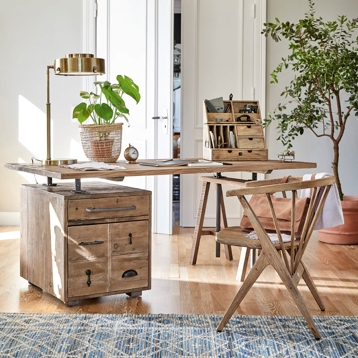 Bureau en bois avec tiroirs et poignées métalliques, lampe dorée et plante verte en pot tressé