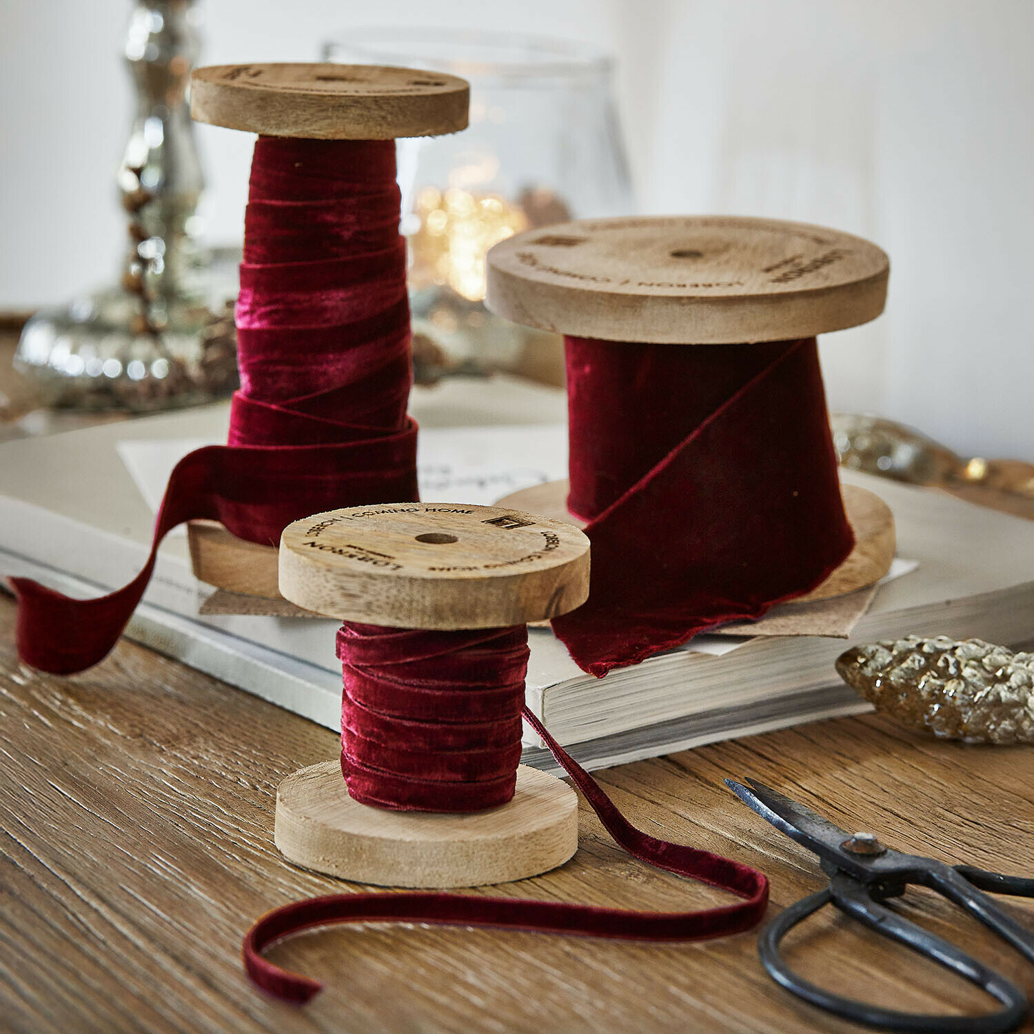 Lot de 2 bobines de ruban en velours Liandis Trois bobines en bois avec ruban en velours bordeaux sur une table en bois avec des ciseaux décoratifs