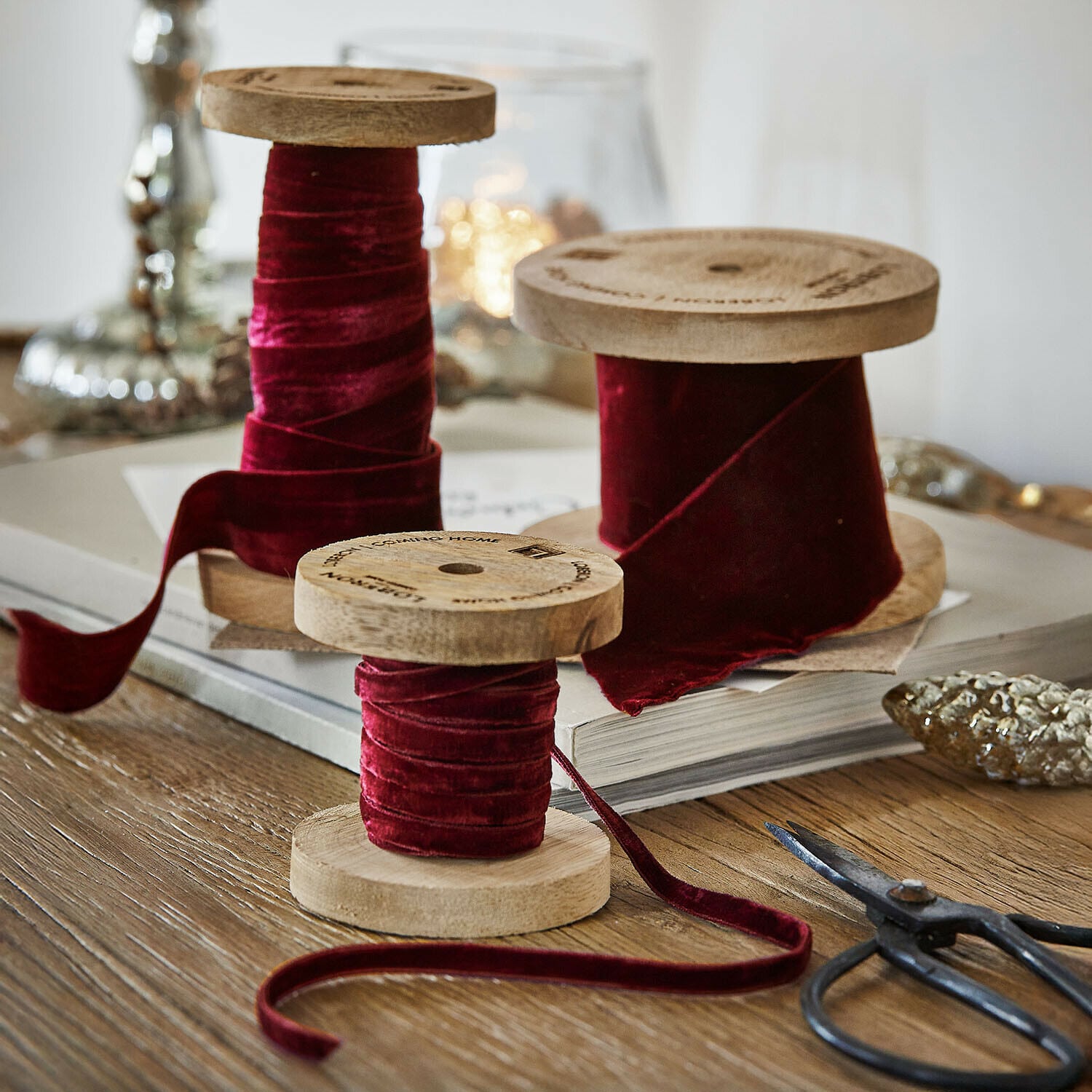 Lot de 2 bobines de ruban en velours Liandis Trois bobines en bois avec ruban en velours bordeaux sur une table en bois avec des ciseaux décoratifs