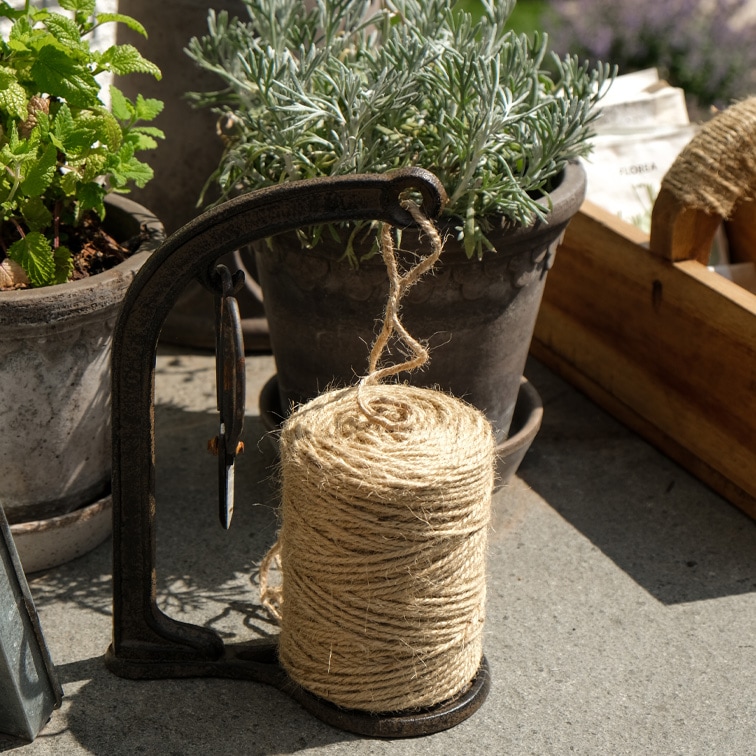 Bobine de corde en jute naturelle sur support métallique près de pots d'herbes pour jardinage