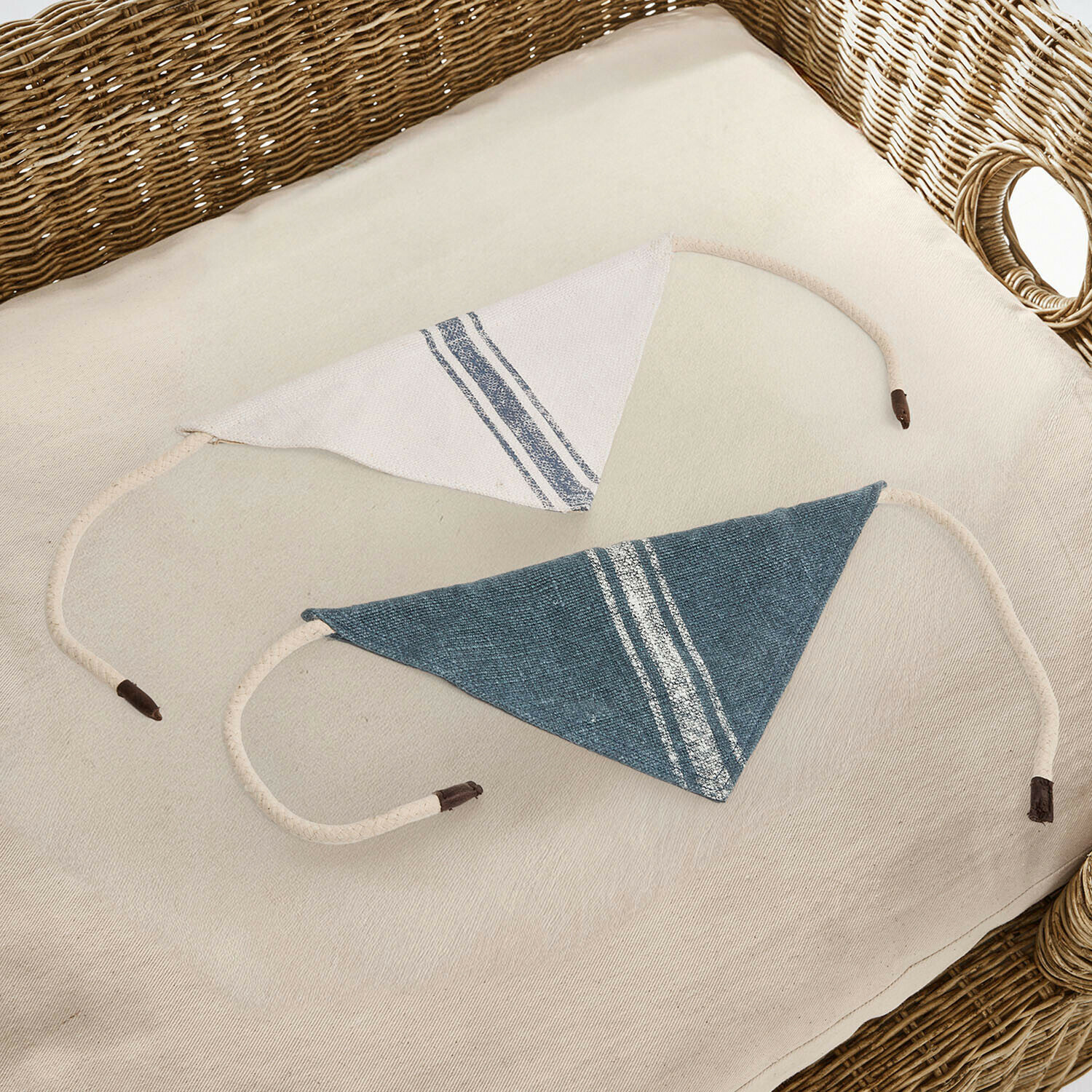 Deux protège-épaules triangulaires en coton blanc et bleu avec rayures posés sur un fauteuil en osier