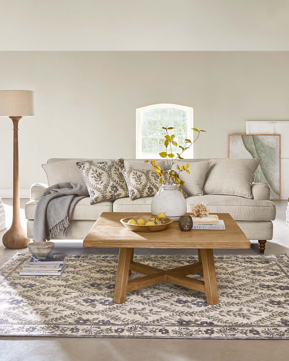 Salon chaleureux avec canapé beige, table basse en bois et tapis décoratif à motif de feuilles