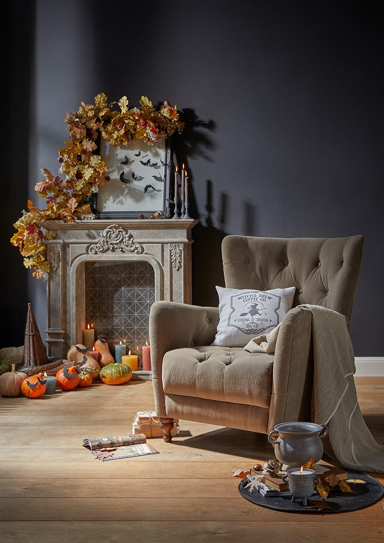 Fauteuil beige rembourré avec coussin et plaid près d'une cheminée décorée d'automne avec citrouilles