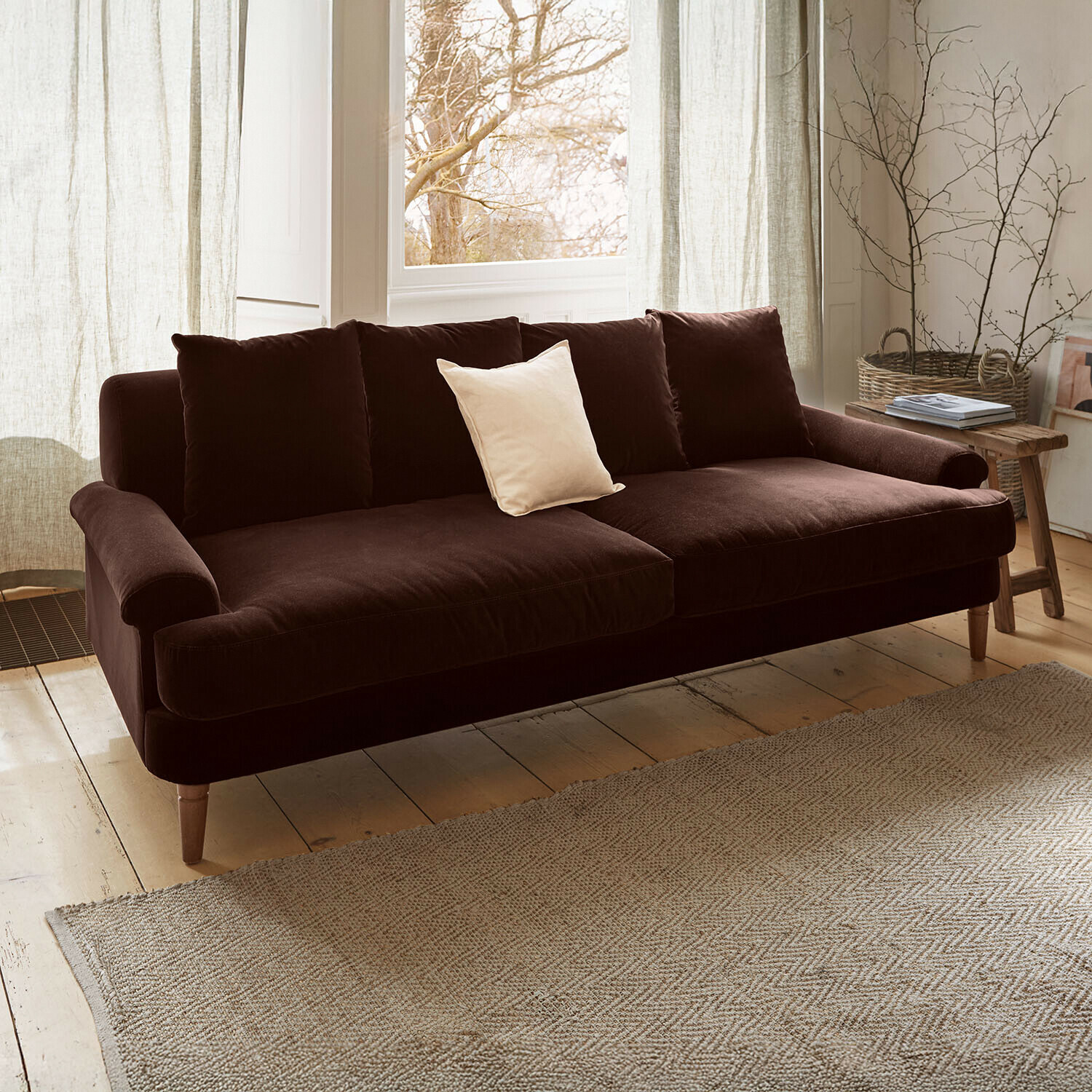 Canapé Rivermere Canapé en velours marron avec coussin clair dans un salon lumineux et chaleureux