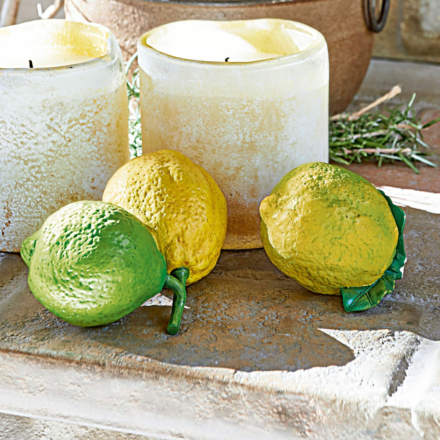 Lot de 2 citrons décoratifs Ginny Citrons décoratifs en plastique vert et jaune posés sur un comptoir en pierre avec des bougies