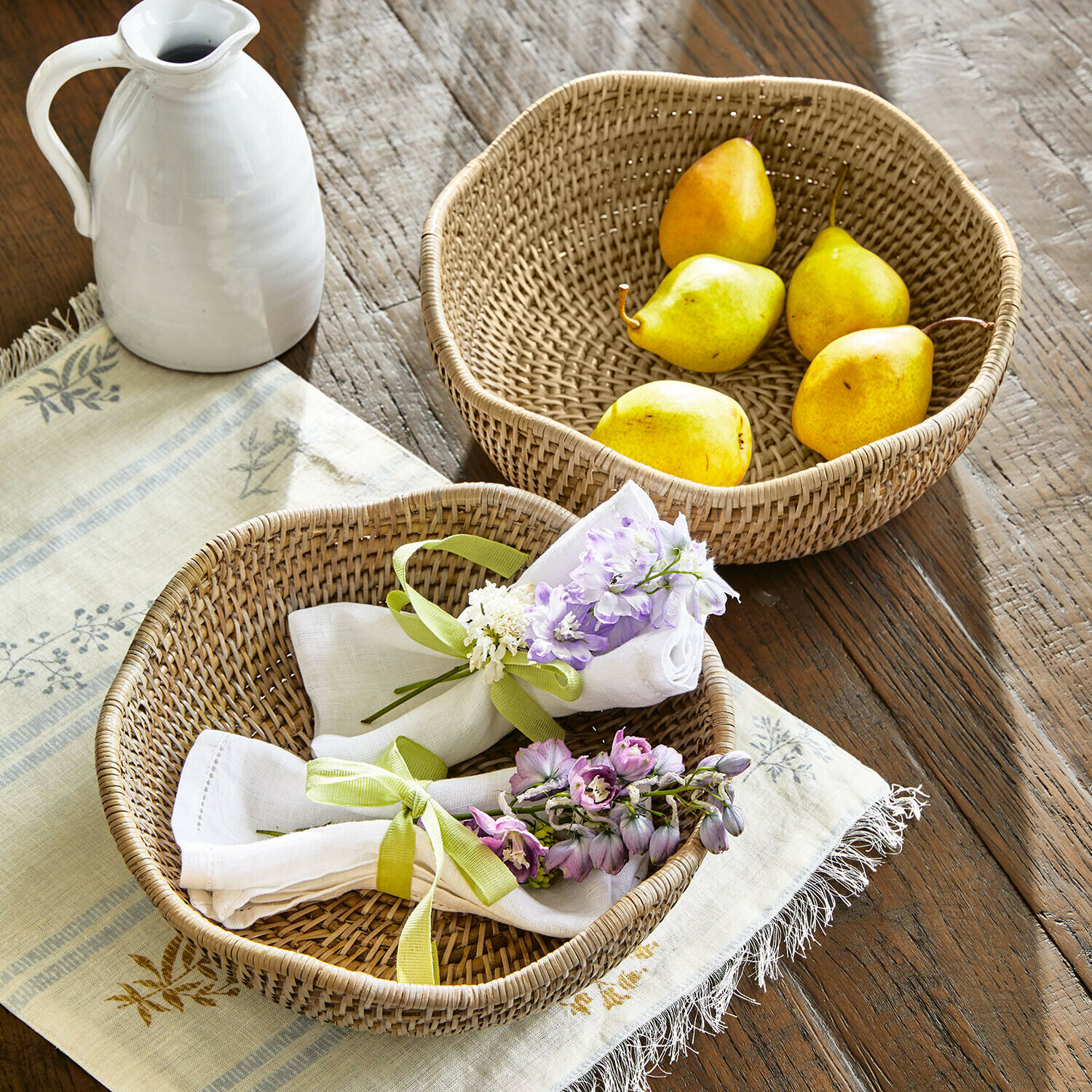 Lot de 2 corbeilles Seravoux Deux paniers ronds en rotin sur une table en bois, l'un avec des poires, l'autre avec des serviettes et des fleurs