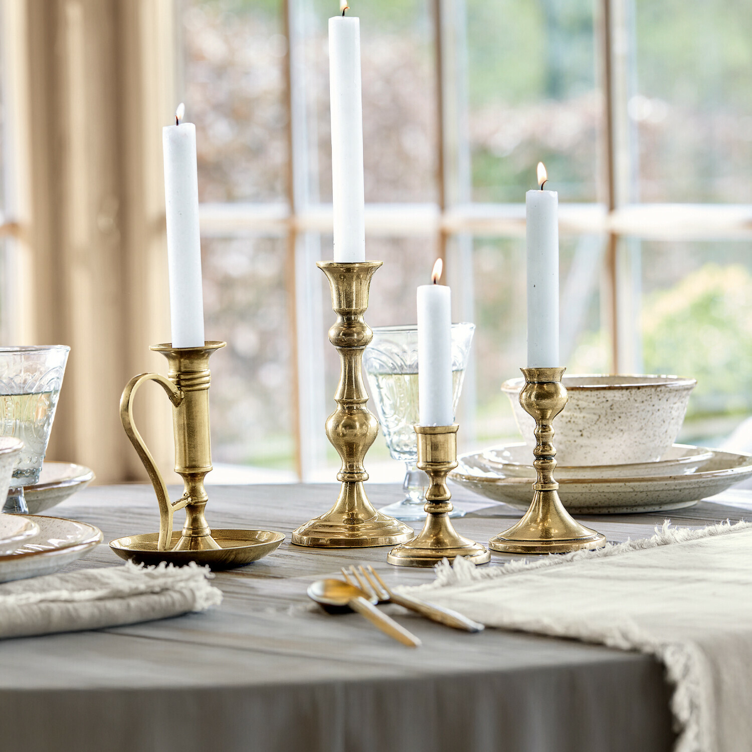 Lot de 4 bougeoirs Maxéville Ensemble de quatre chandeliers en laiton avec bougies blanches sur une table en bois dans une salle à manger