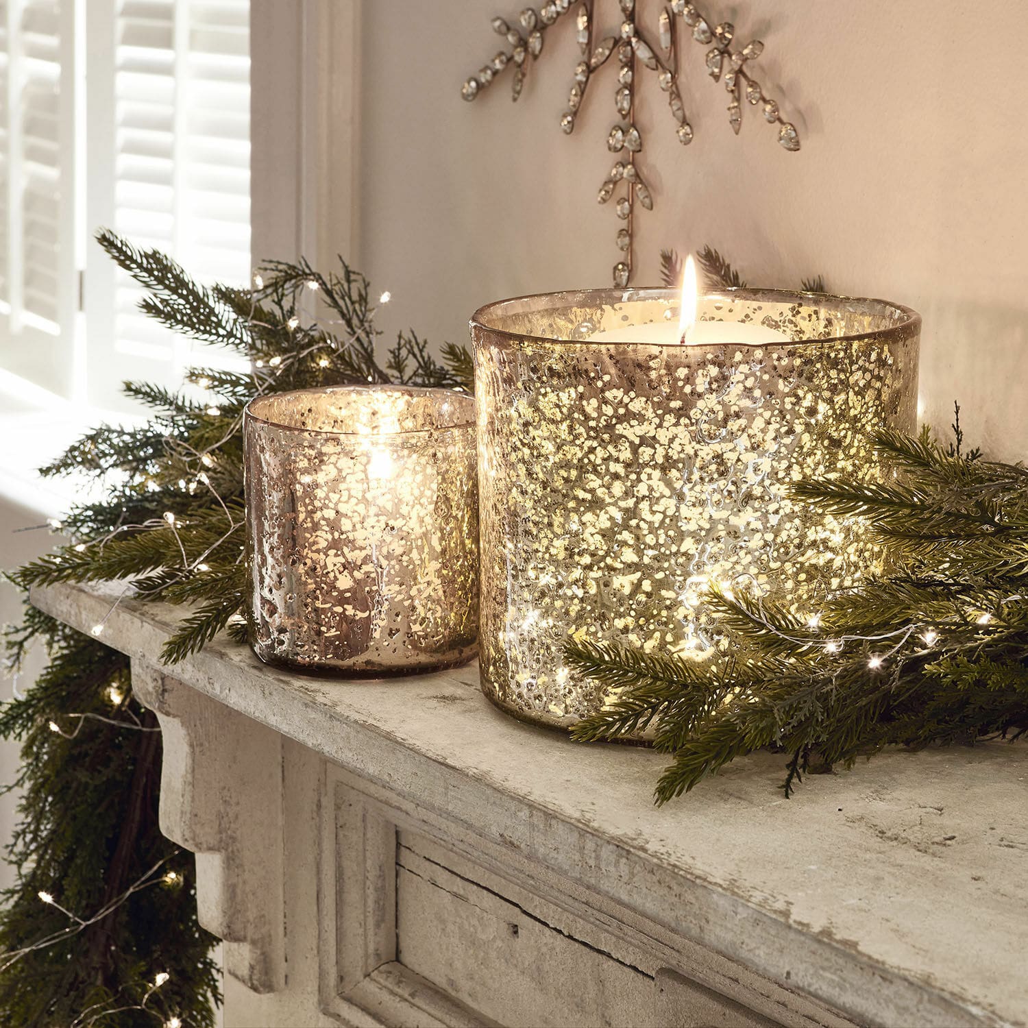 Lot de 2 photophores Samuel Deux photophores en verre effet argent vieilli sur une cheminée avec branches vertes et guirlandes lumineuses