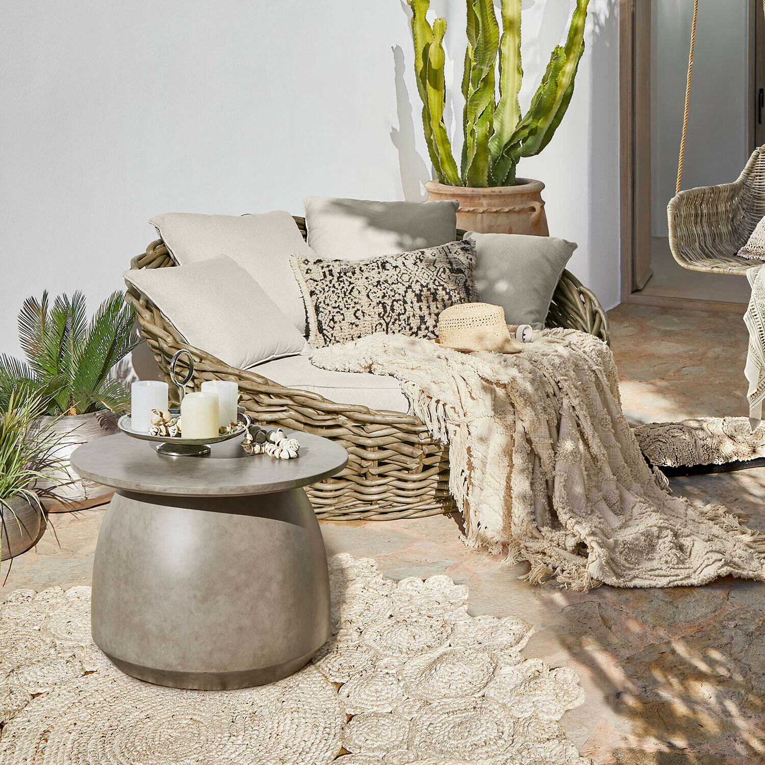 Canapé rond en rotin avec coussins crème et plaid sur terrasse avec table basse en béton